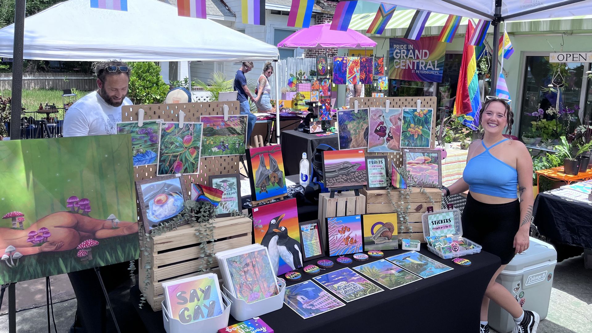 A woman stands to the right of a table with paintings and prints of Florida nature scenes and animal and plant life.