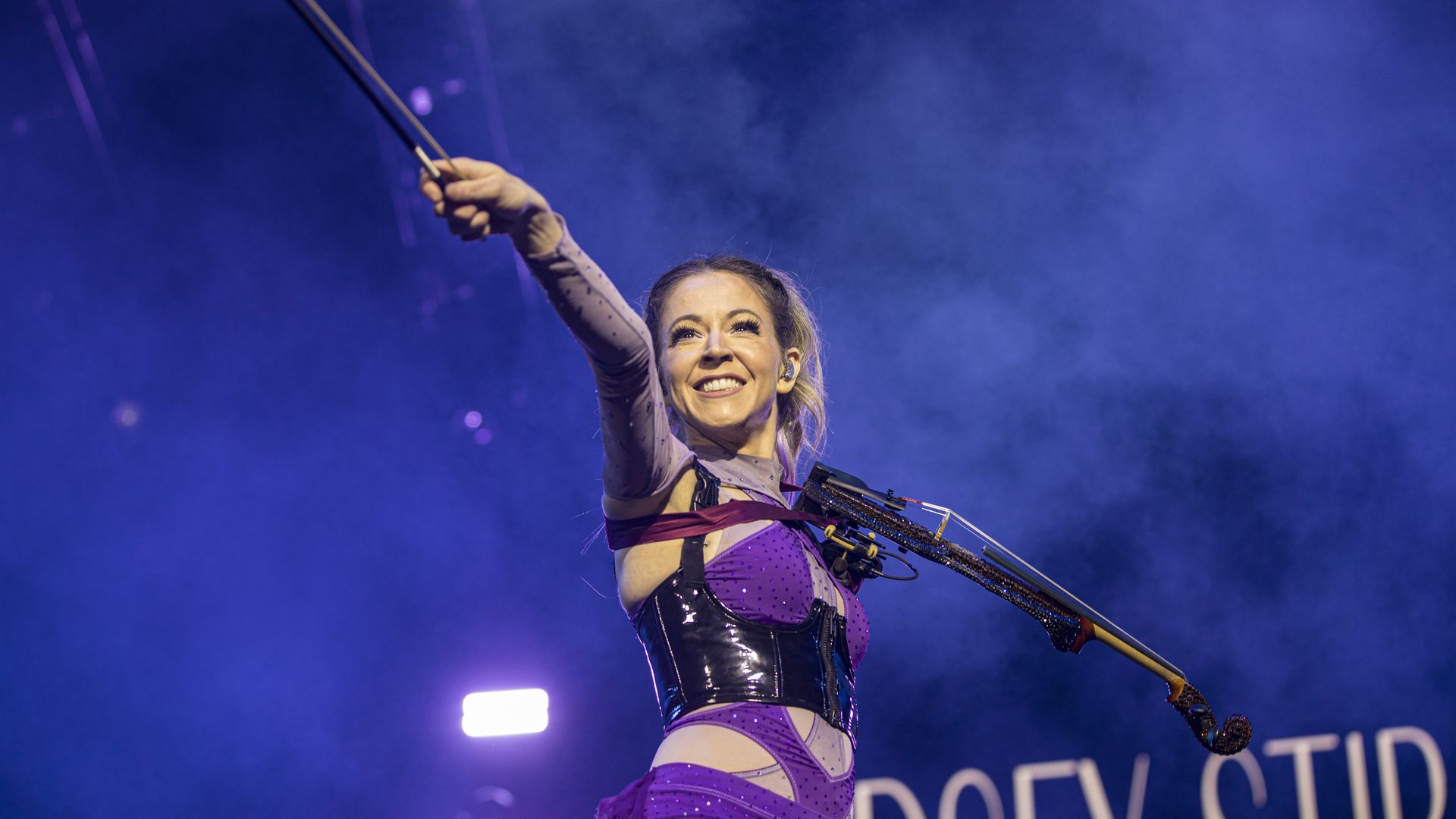 Photo shows Lindsey Stirling a purple outfit with a violin.