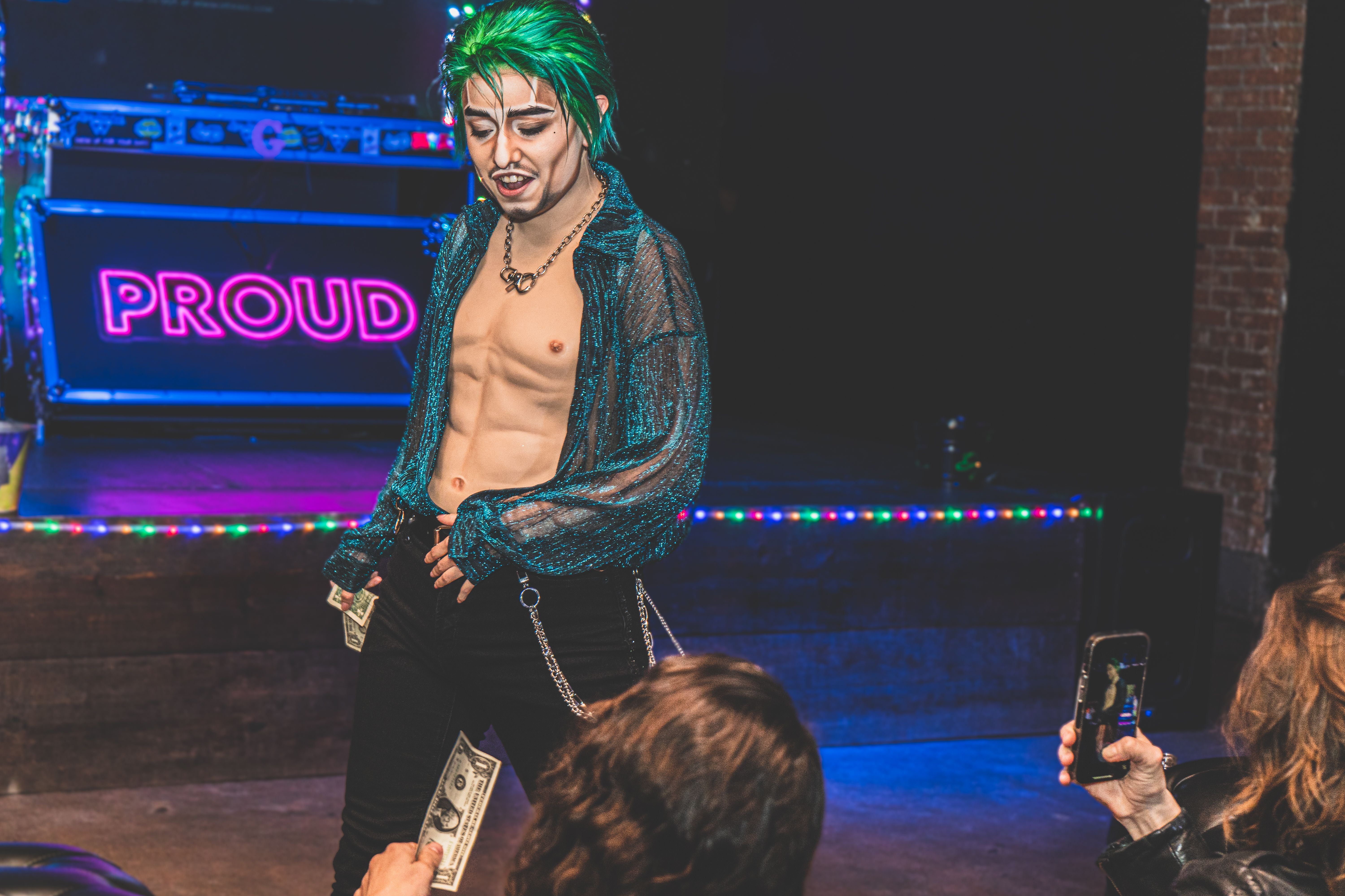 Photo of a drag king wearing a green wig and a blue button-up shirt open