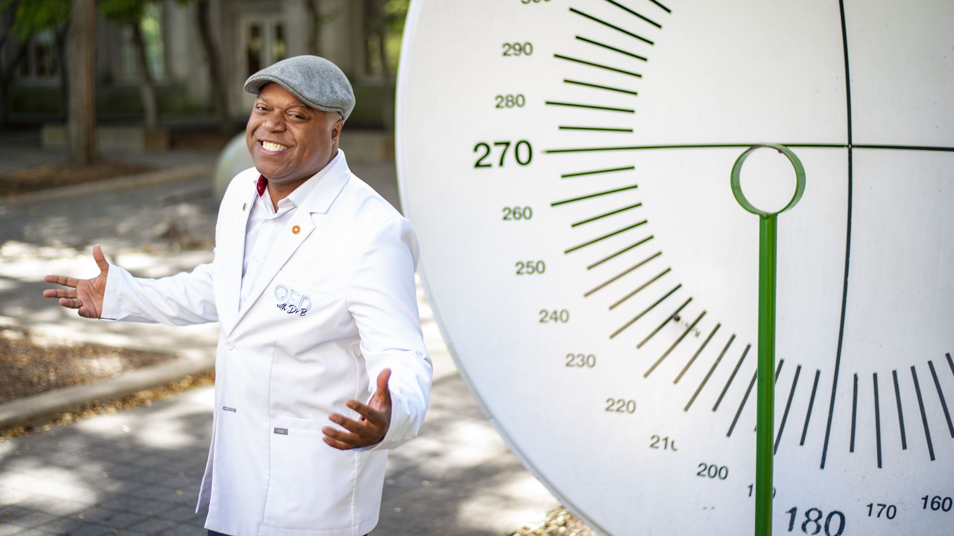 Frederic Bertley poses in a white lab coat next to a "whisper disc" outside COSI