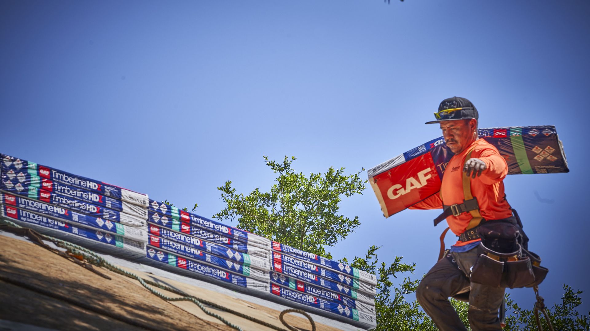 A roofer hauls shingles on a rooftop.