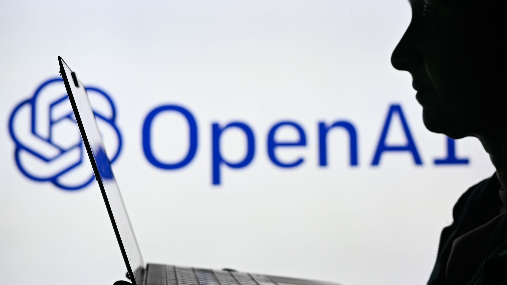 An image of a woman holding a laptop in front of an OpenAI logo displayed on a computer screen.