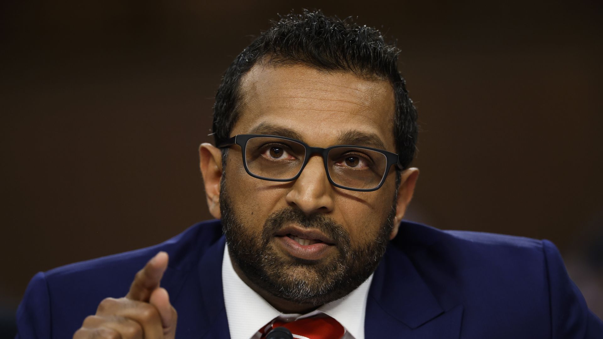 Kash Patel speaking in a blue jacket, white shirt and red tie 