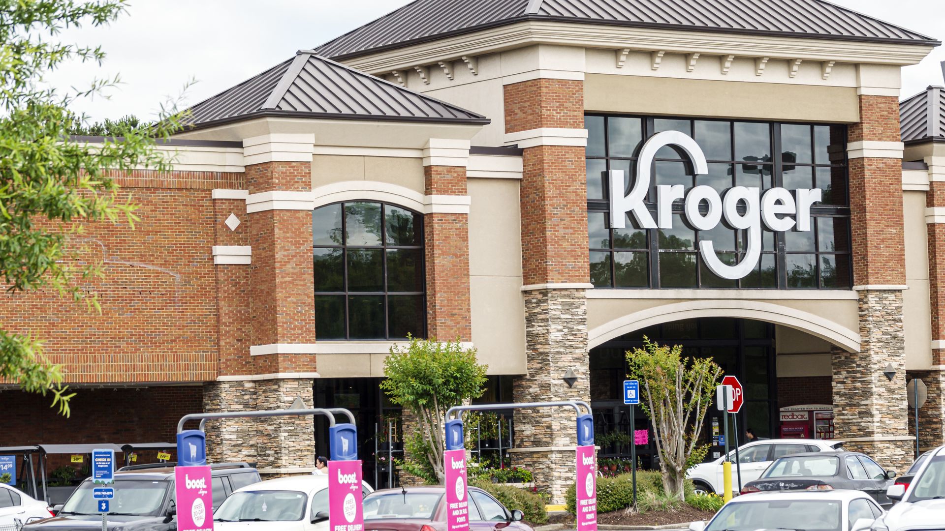 Customers enter a Kroger grocery store, which has a brick and glass facade.