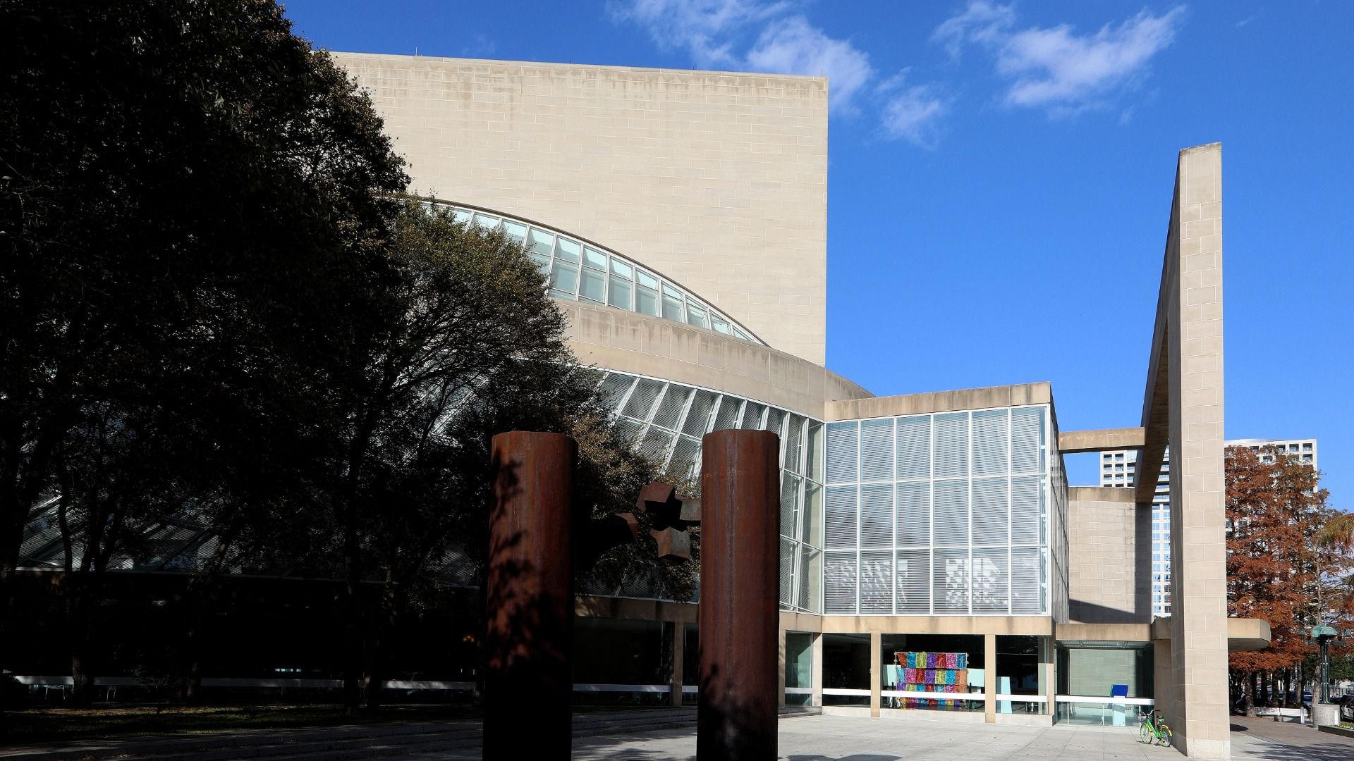 The Morton H. Meyerson Symphony Center is a modern building with large curved glass windows and stone walls. 
