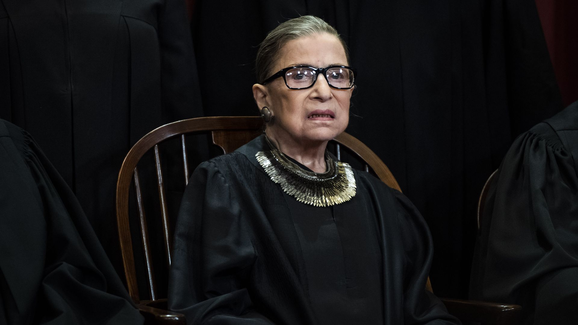 In this image, Justice Ruth Bader Ginsburg sits in a chair. 