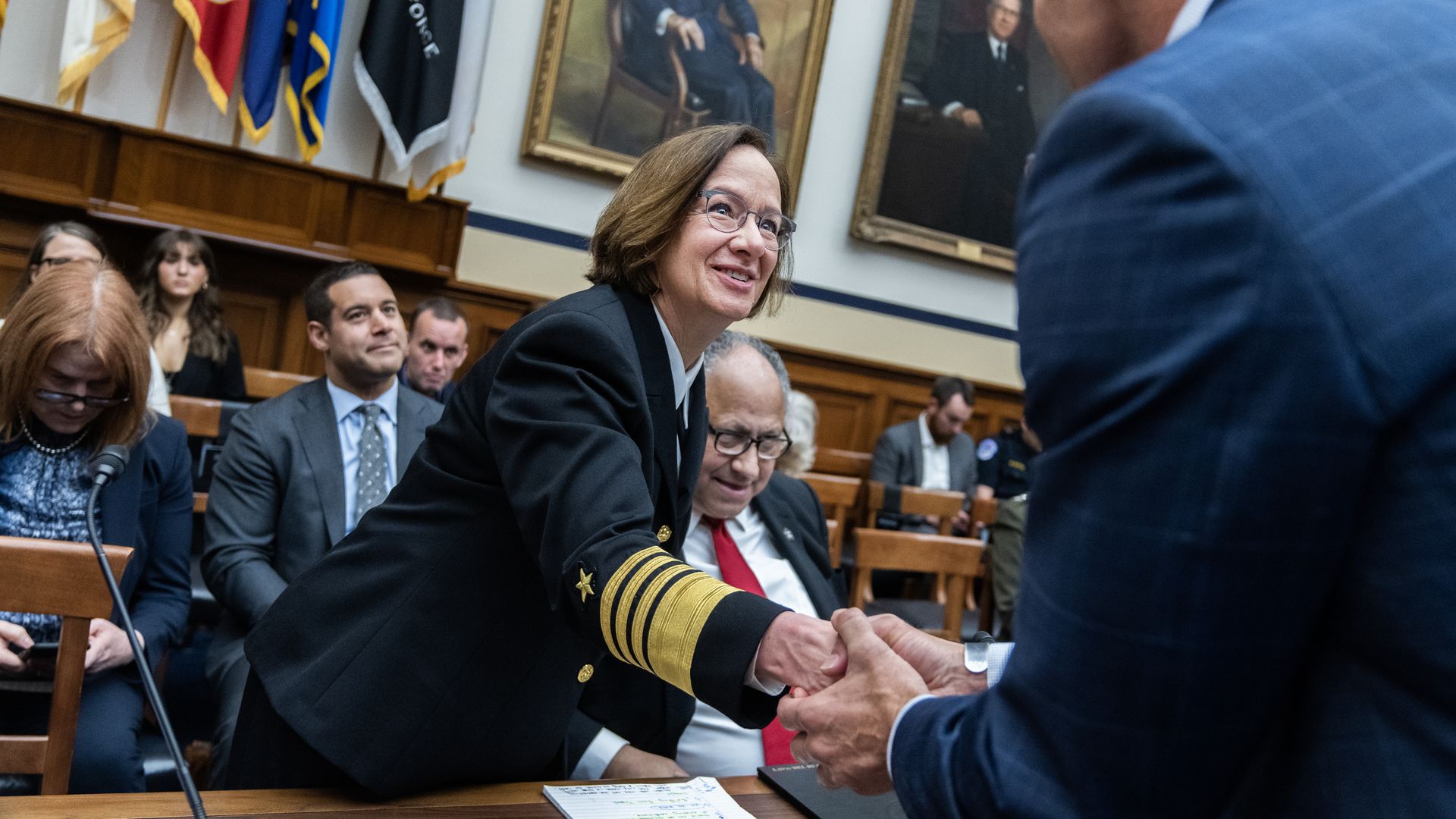 Adm. Lisa Franchetti, in her dress uniform, shakes hands with a lawmaker. Navy Secretary Carlos Del Toro is seated behind her.