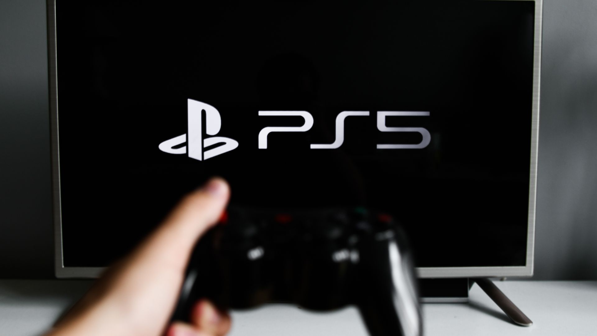 Photo of a TV with a PS5 controller on it. A controller also appears, held by someone off-camera