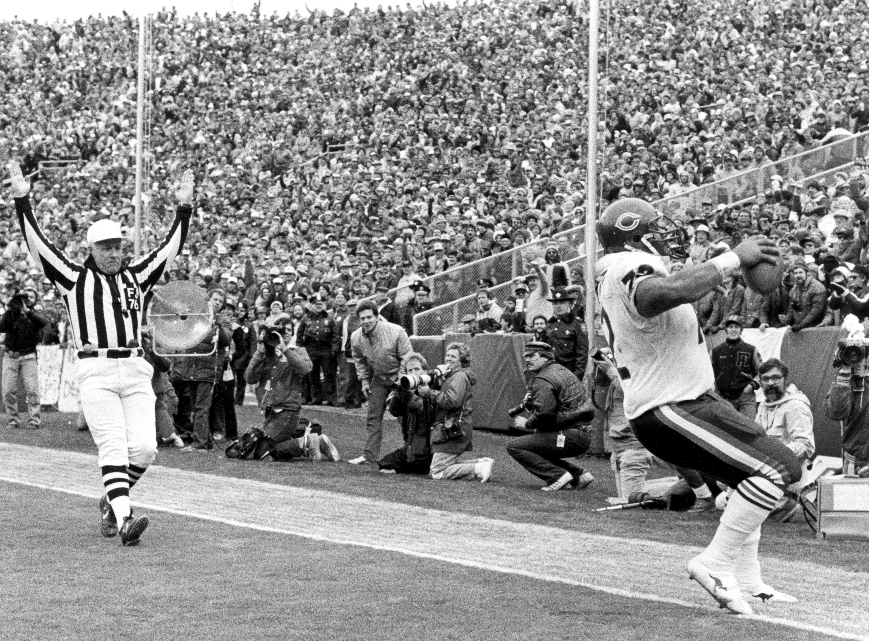 Black-and-white photo of a Chicago Bears player scoring a touchdown while a referee raises both arms and photographers capture the moment in a packed stadium.