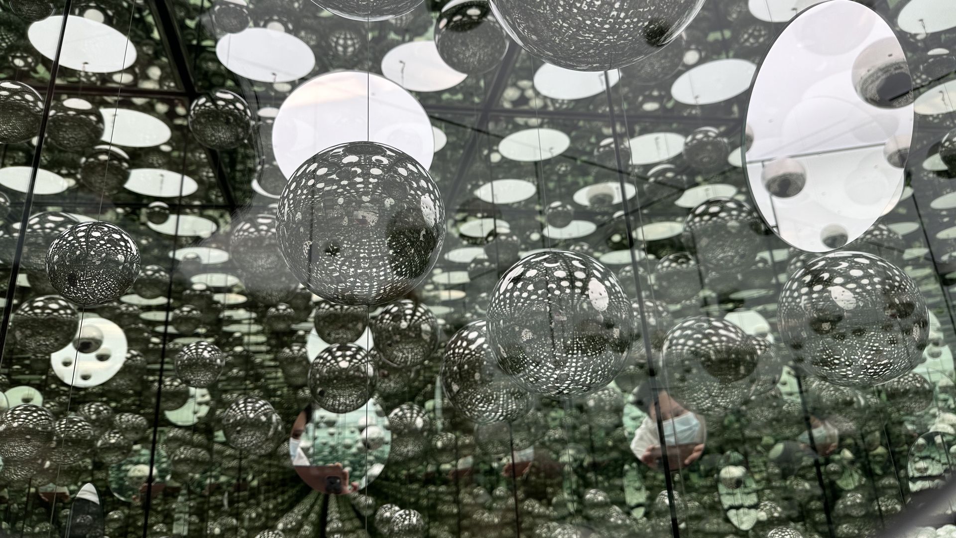 As part of an art installation by Yayoi Kusama, the view inside a mirrored box within a mirrored room, both filled with stainless steel, inflatable spheres. 