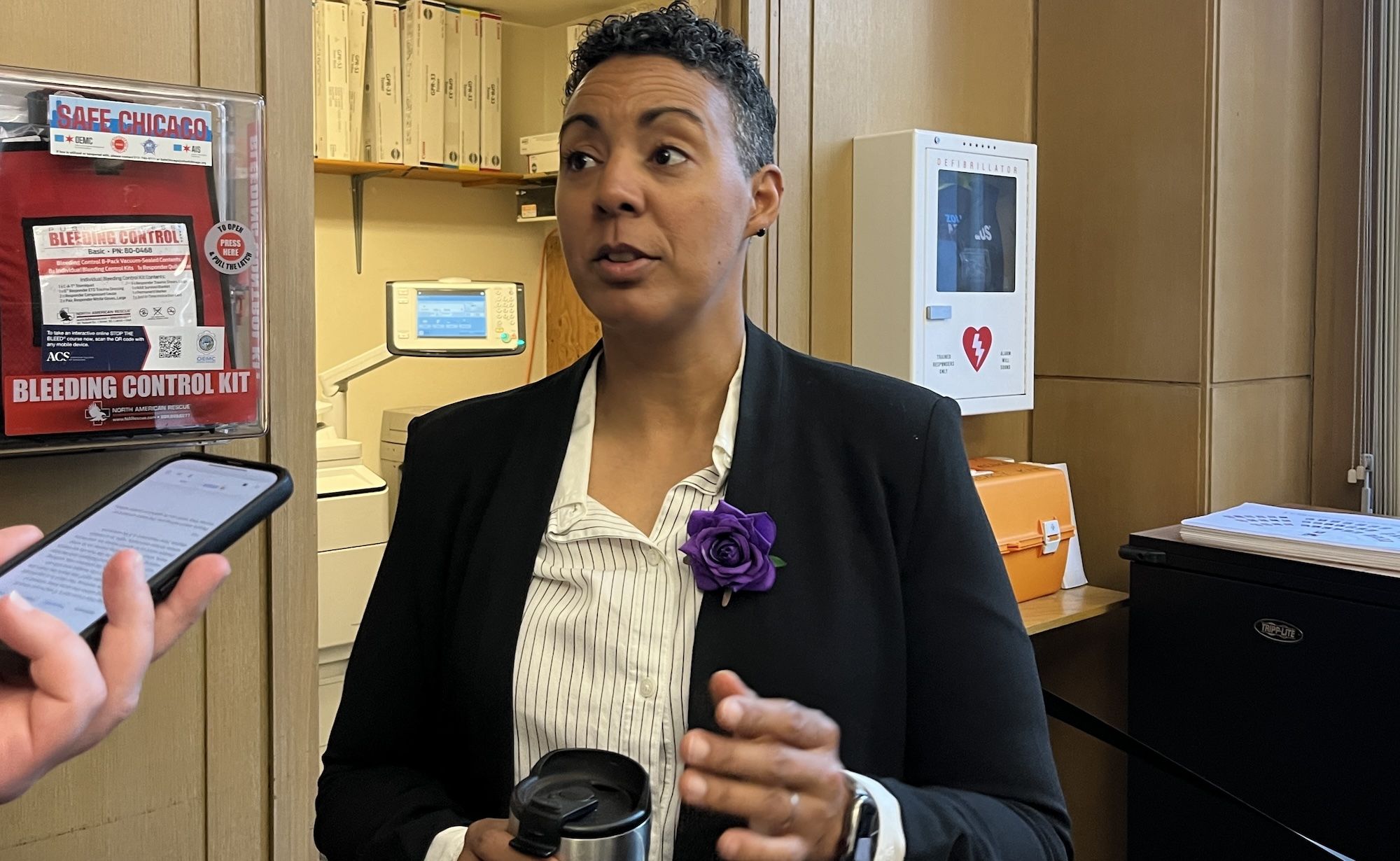 Woman in suit with purple flower talking to someone with a phone.
