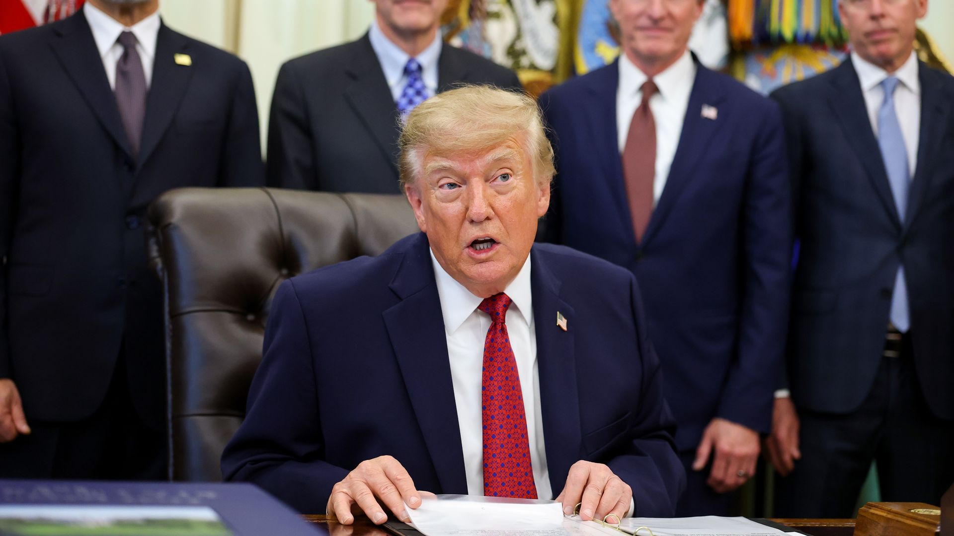 President Trump seated in the Oval Office, surrounded by Cabinet secretaries.