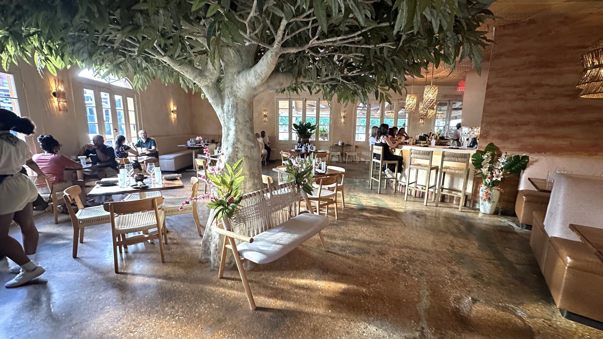 The interior of a restaurant with a faux tree planted at the middle.