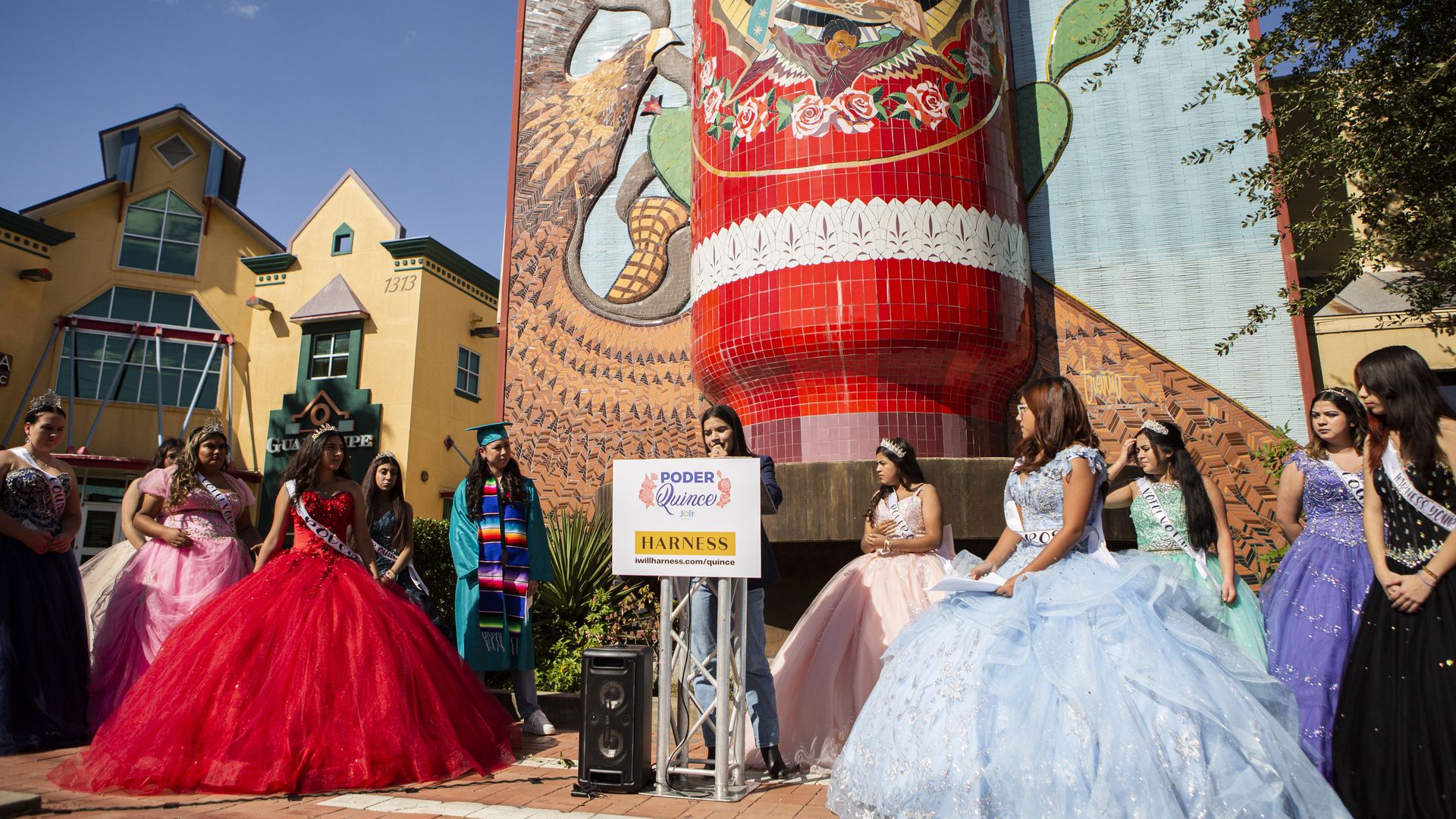 Actress America Ferrera stands at a press conference surrounded by teen girls wearing colorful quinceañera gowns.