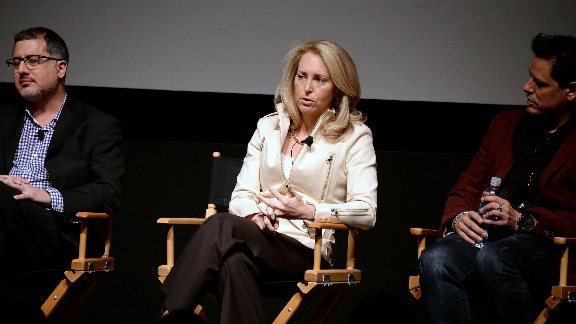 In this image, Plume sits in a chair and speaks on stage between two other seated people.