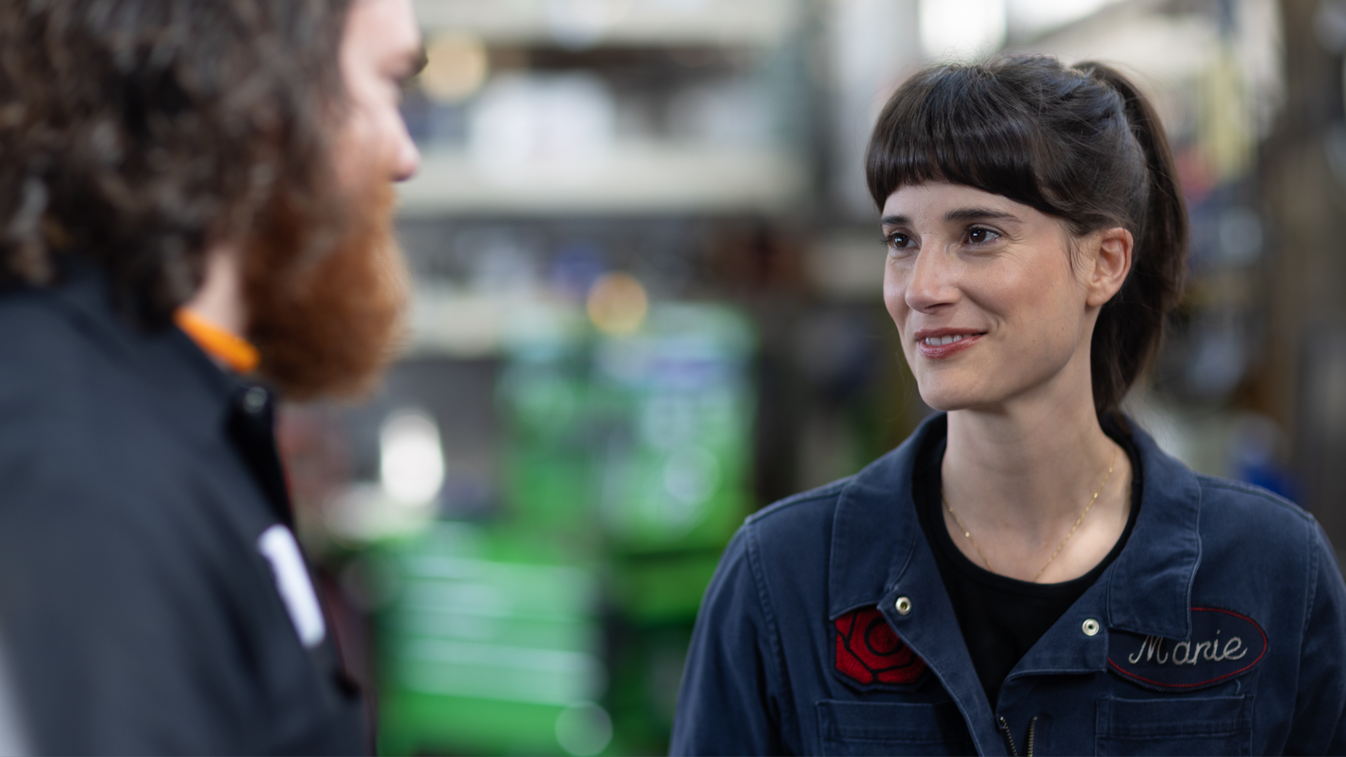 A woman in coveralls looks at someone else who is speaking. 