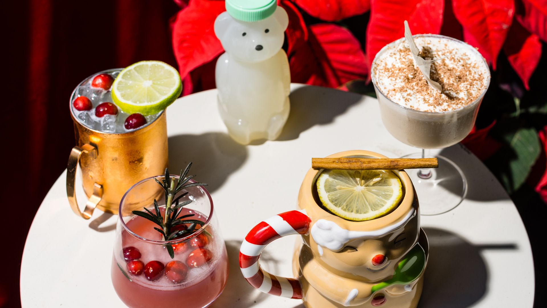 Four drinks, some in holiday glasses, arranged on a white circular table. 
