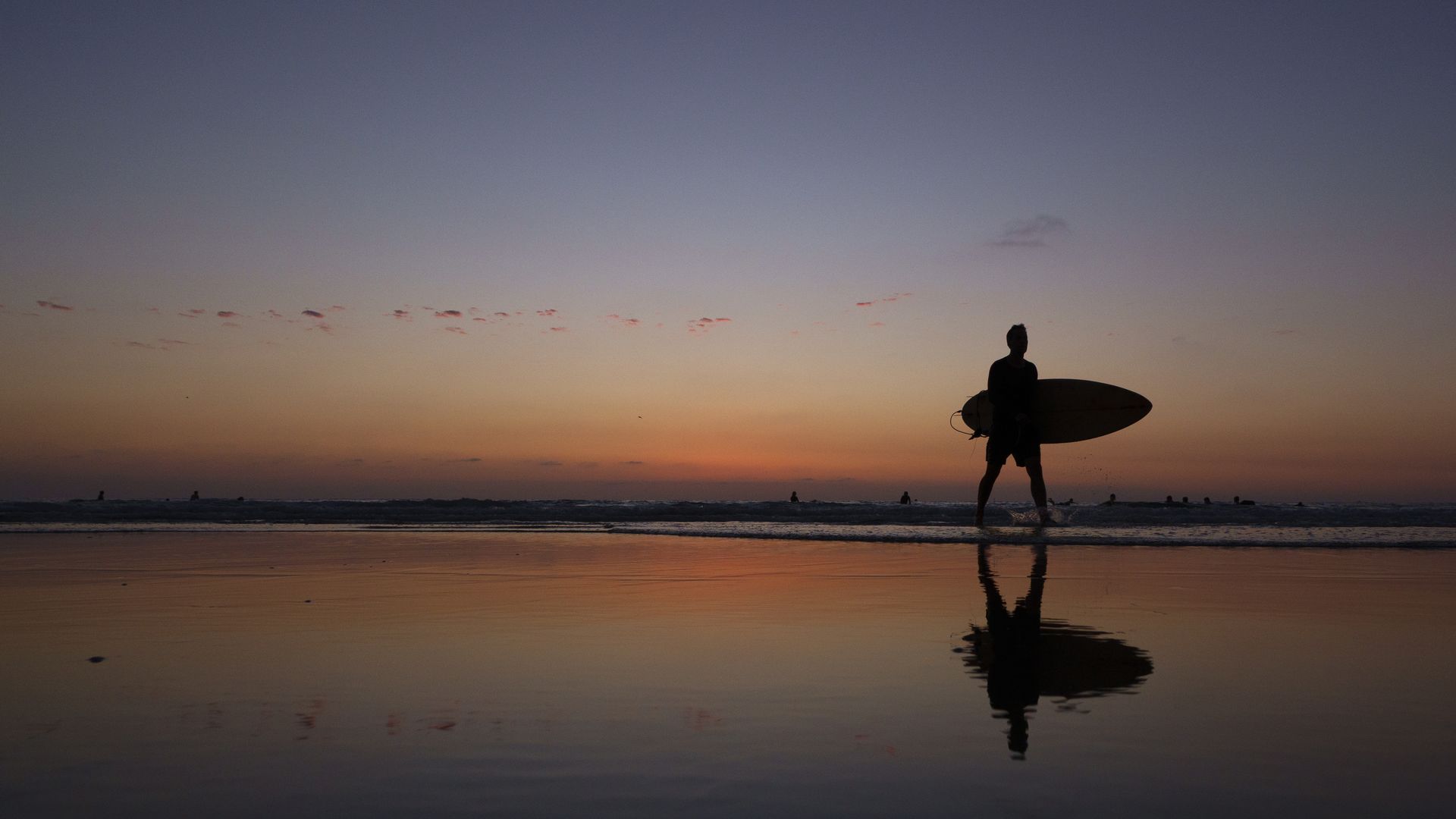  surfer gets out of the Pacific Ocean after surfing at La Jolla Shores beach at sunset on a warm, summer evening on August 26, 2025 in San Diego, California. 