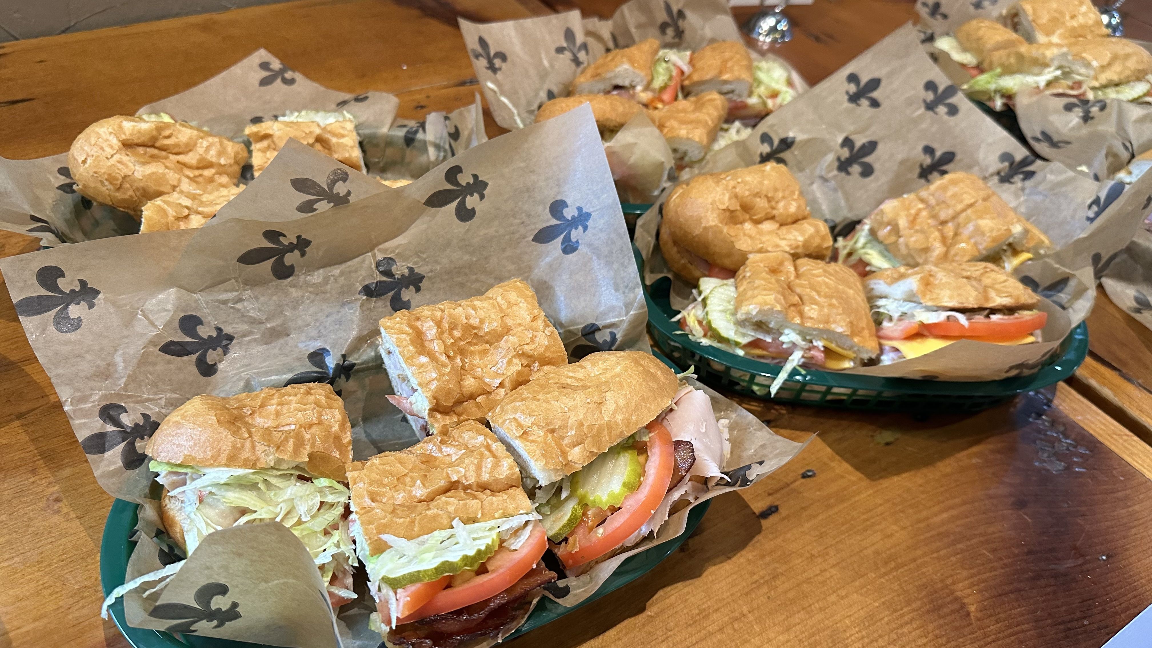 Baskets of poboys sit on a wooden tabletop.