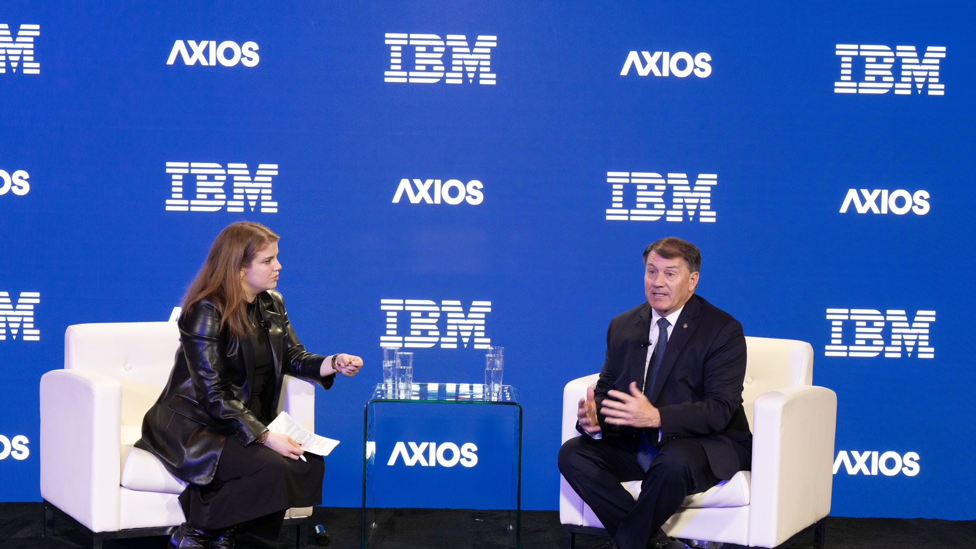 Two people sit on white chairs in conversation