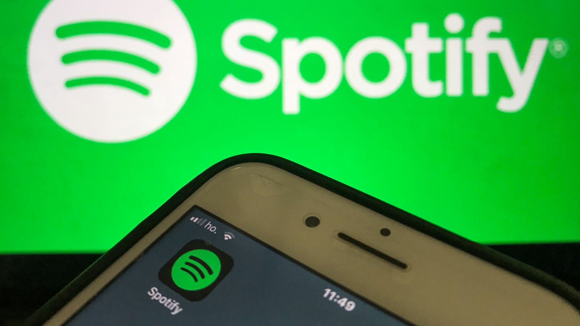 A photo of the Spotify app running on an iPhone with the Spotify logo in the background.