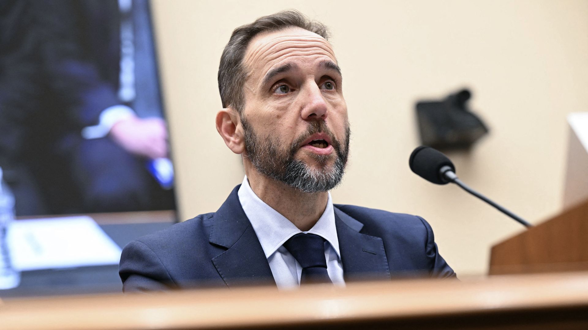 Jack Smith speaks into a microphone while seated 