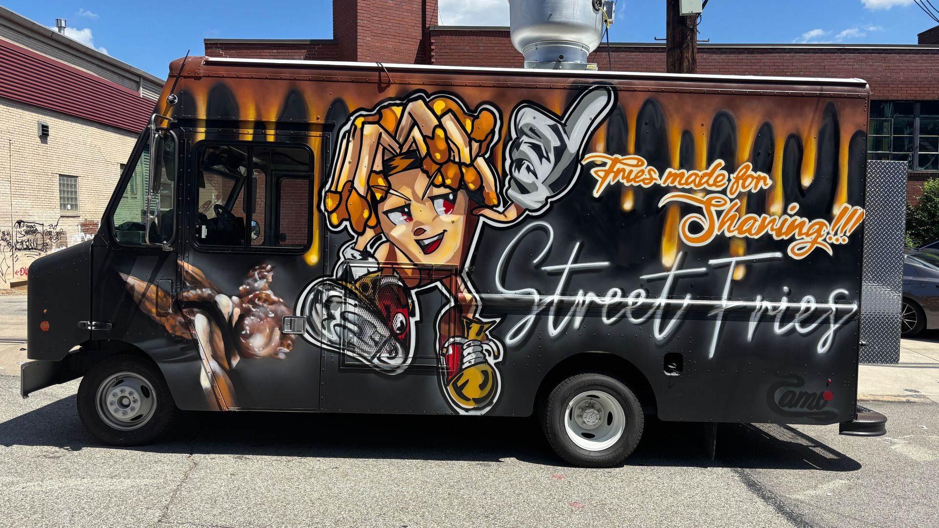 Black food truck with colorful graffiti of a cartoon fries character and a dancer, with orange and white text saying "Fries made for Sharing!!! Street Fries".