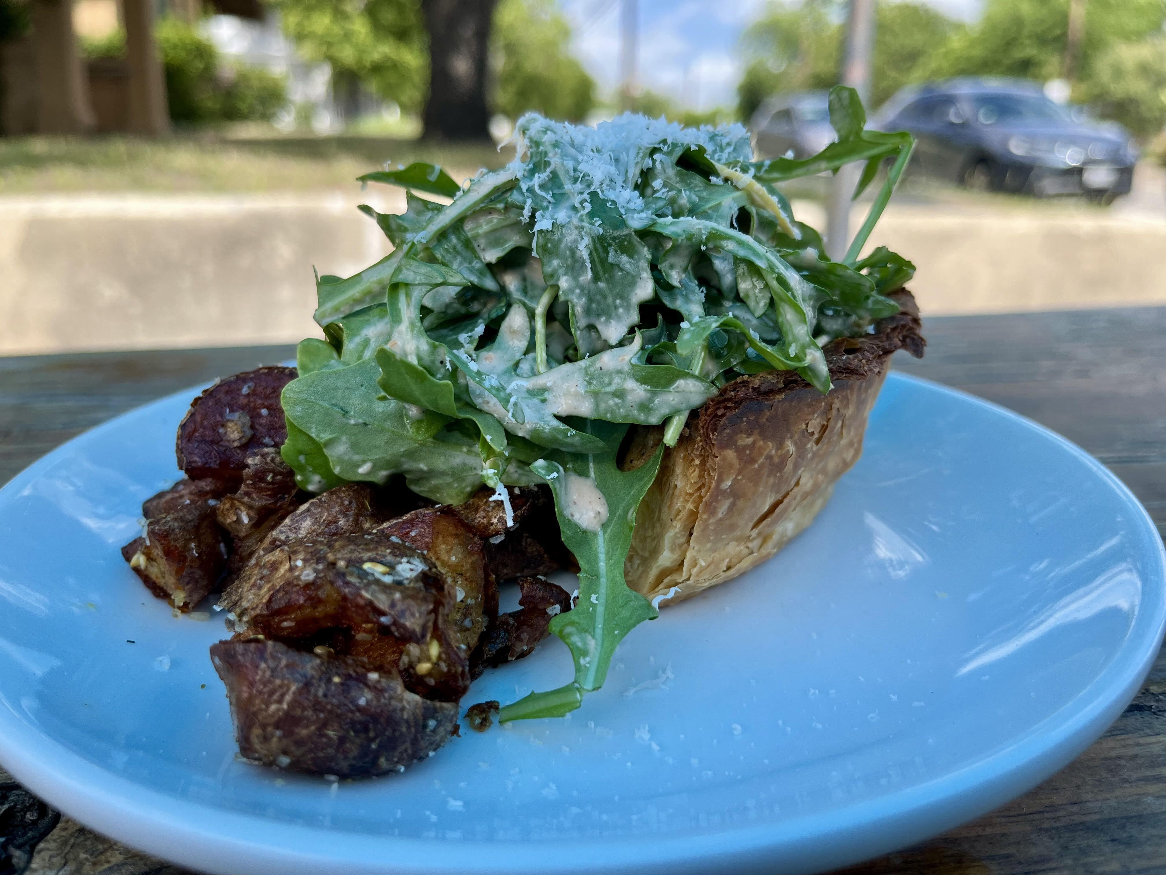 A piece of quiche topped with greens on a white plate.