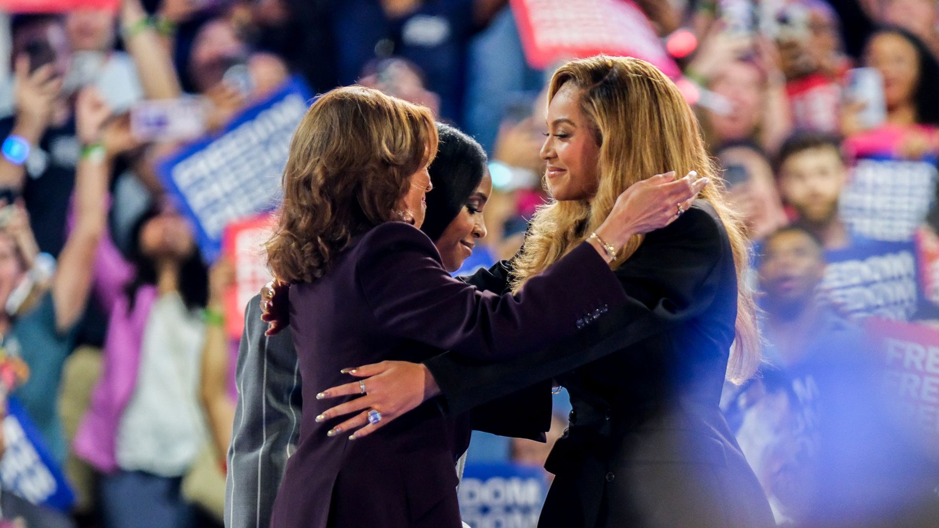 Kamala Harris embraces Beyoncé at a campaign rally while supporters wave signs.