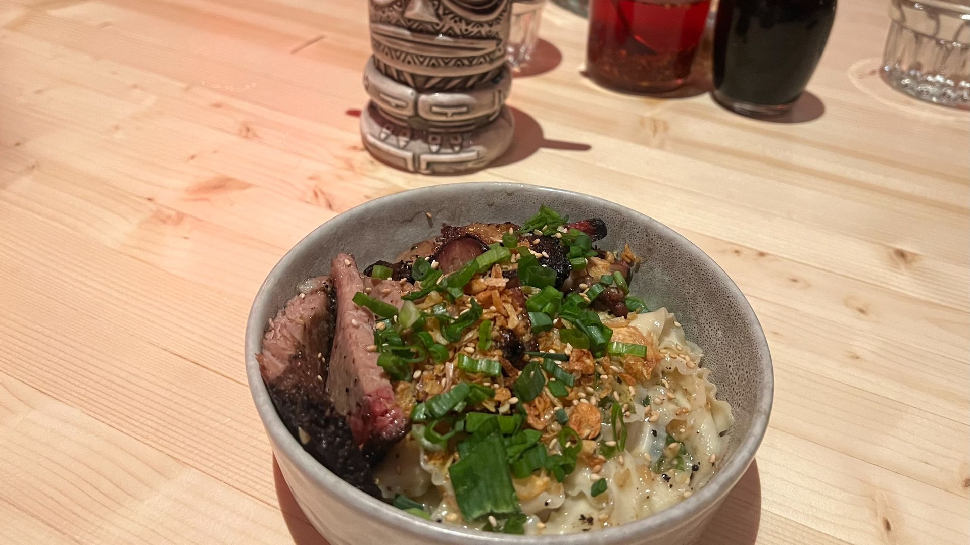 A bowl containing noodles and brisket sits on a wooden table.