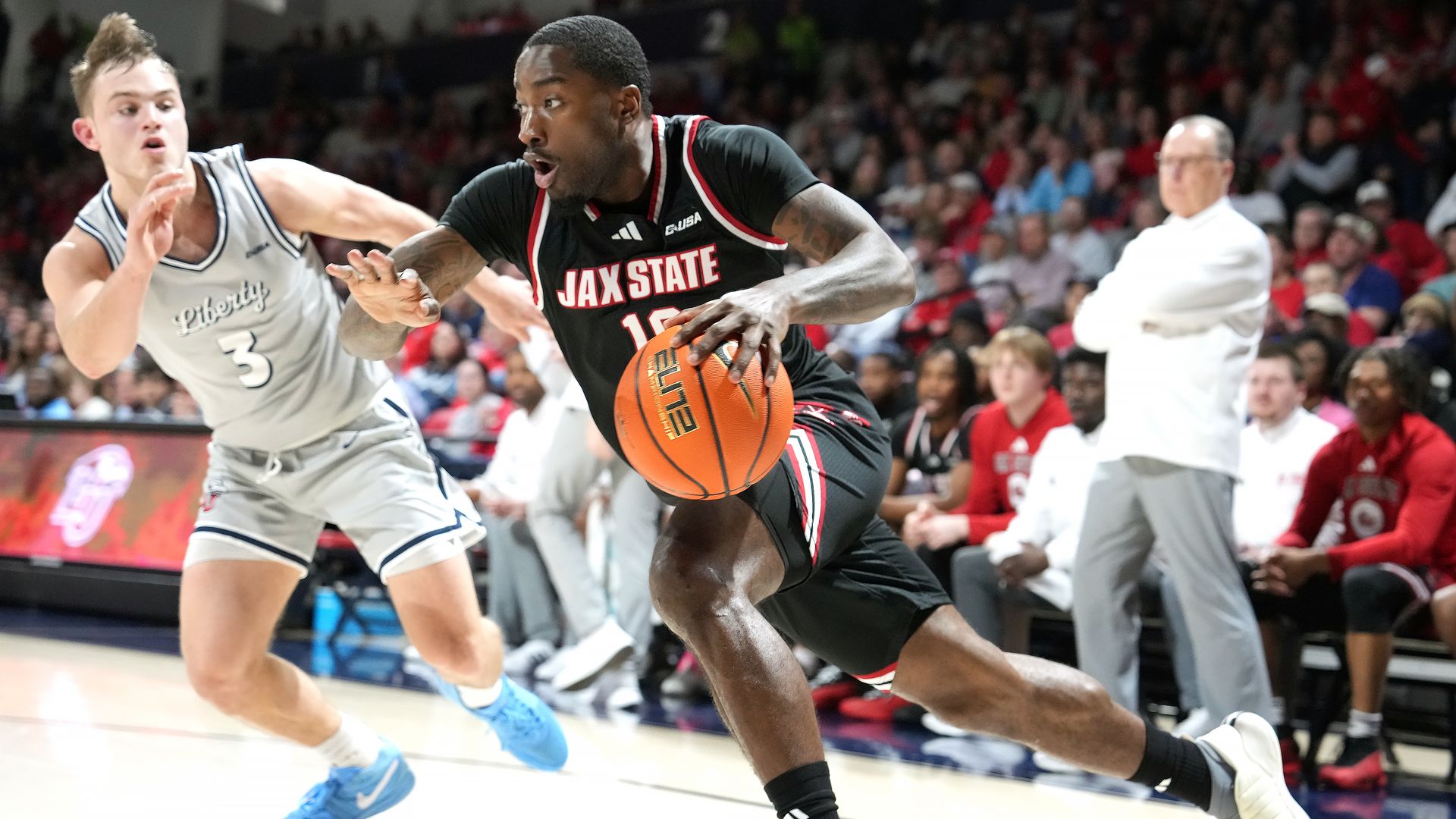 A Jacksonville state basketball player dribbles while a Liberty University player defends. 