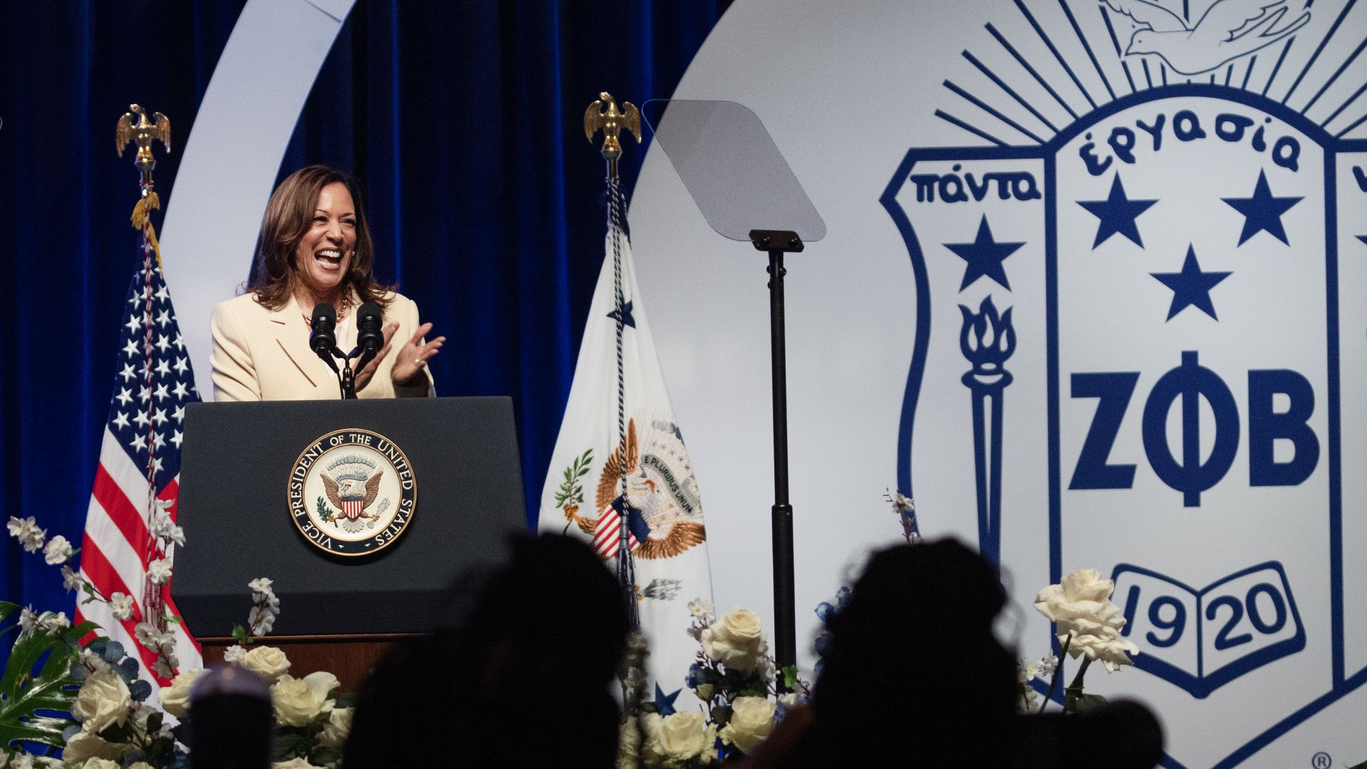 Harris stands on a stage surrounded by flowers, American flag and Zeta Phi Beta letters 
