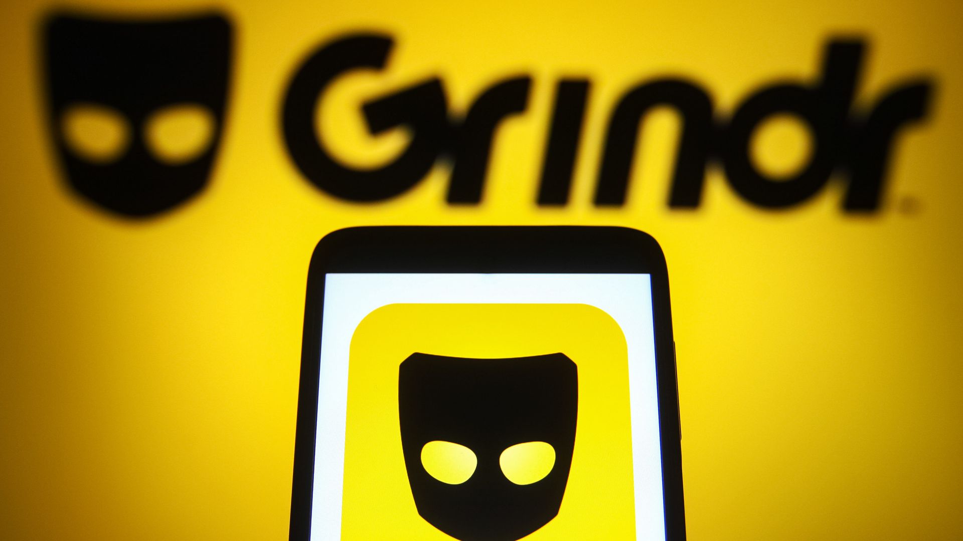 A photo illustration of the Grindr logo on a smartphone and a PC