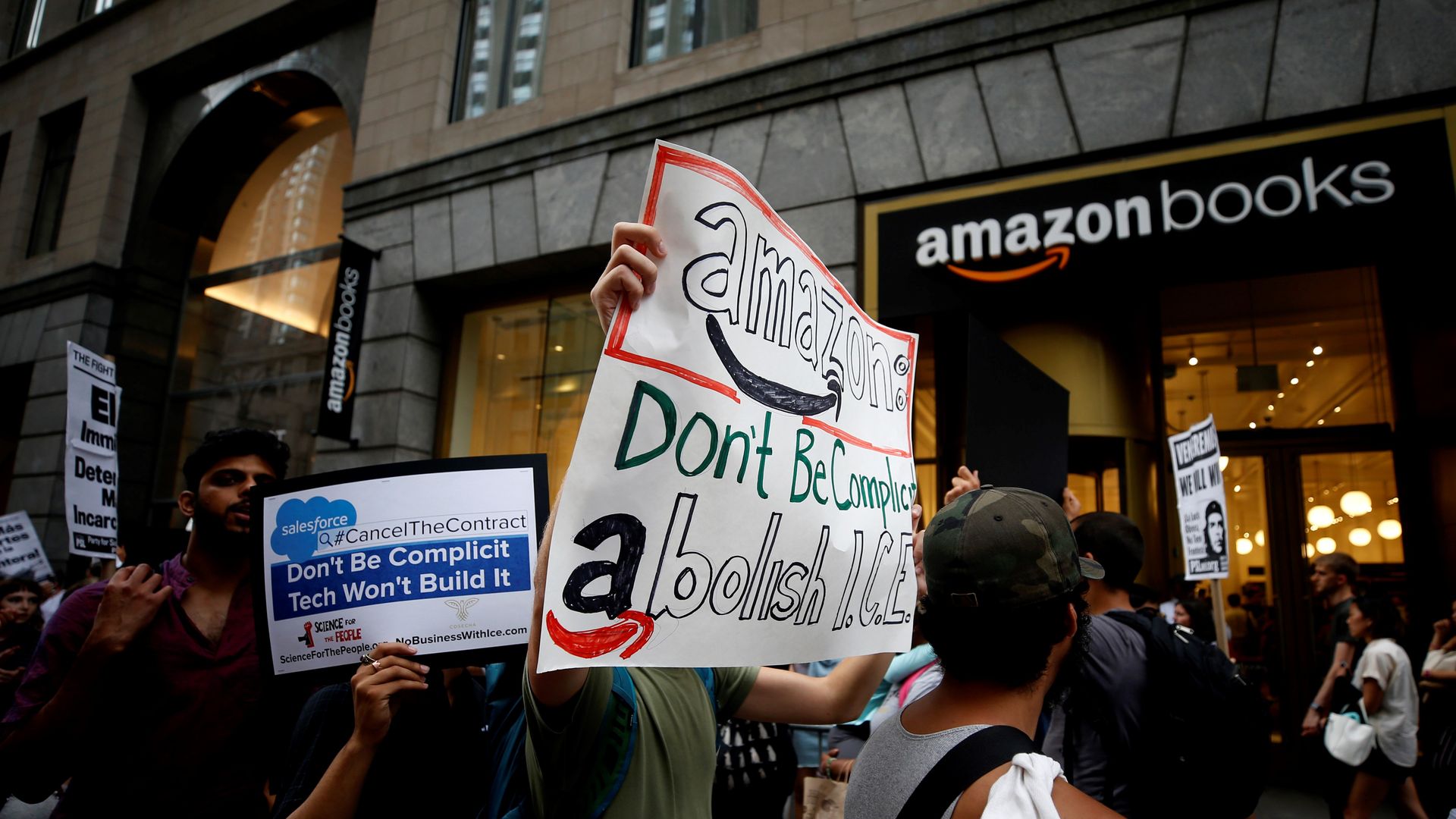 Protesters hold up anti-ICE posters in front of an Amazon bookstore