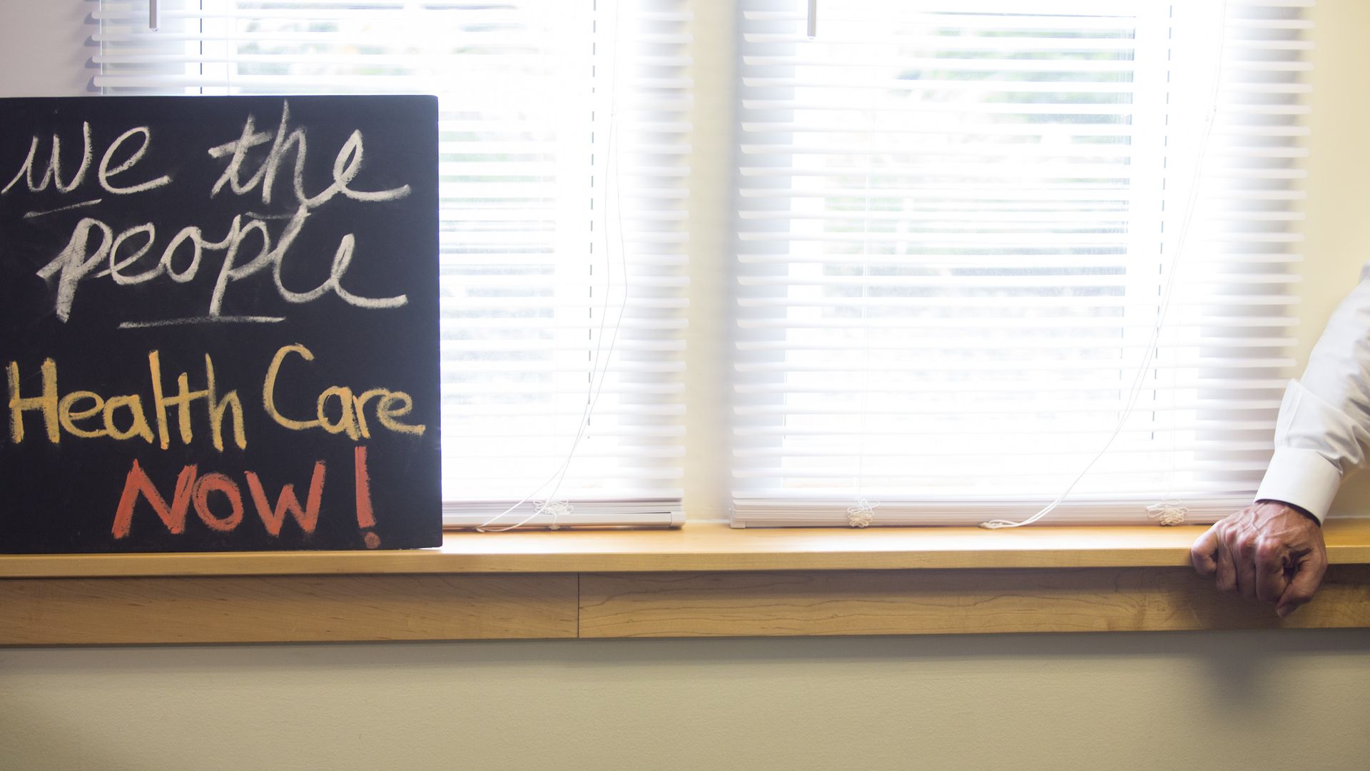 A sign on a window that says "We the people, Health Care now!"