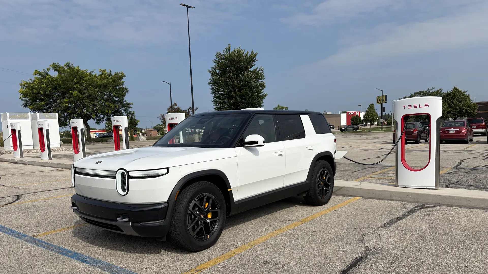 Photo of a Rivian R2 SUV charging at a Tesla Supercharger station.