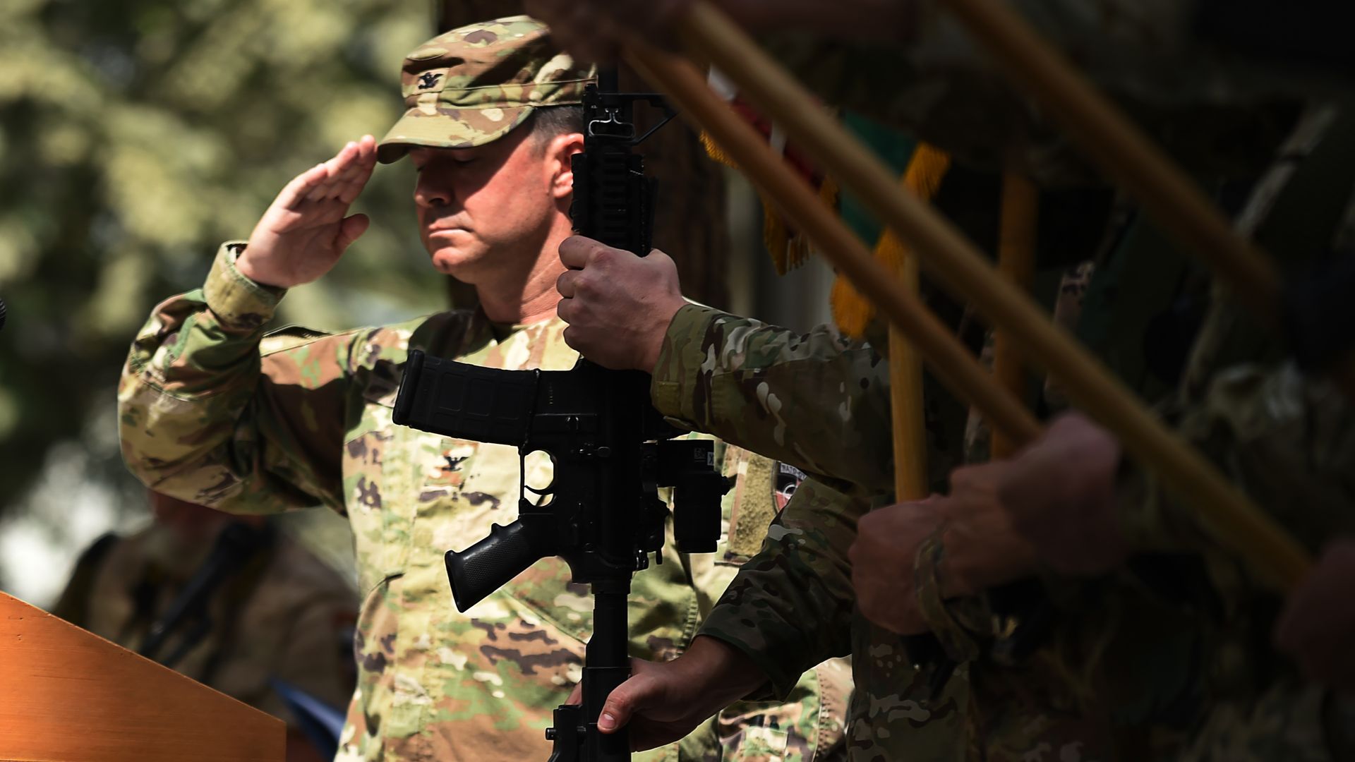 U.S. soldier salutes, behind a silhouette of a gun.