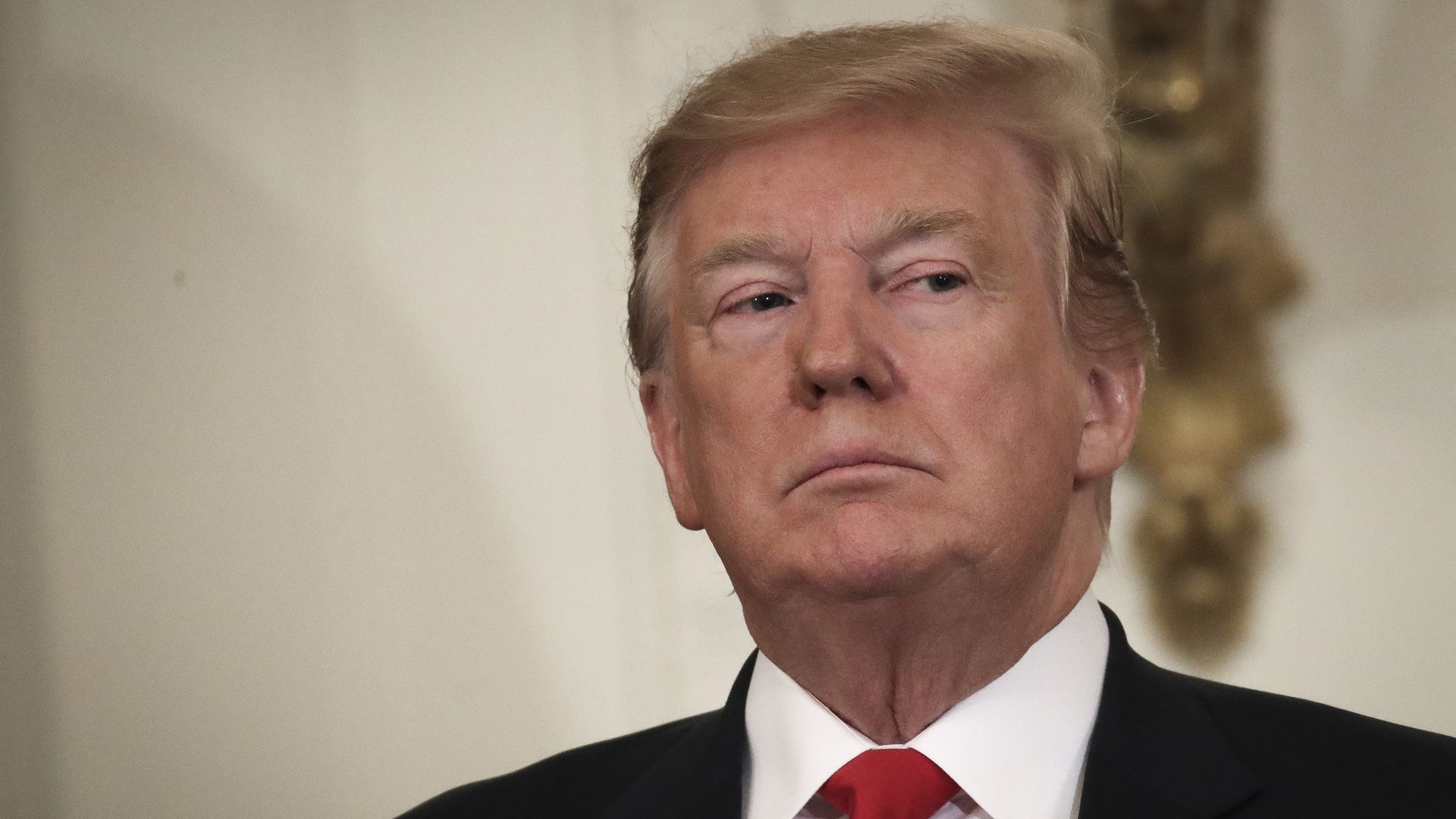 In this image, Trump stands in a red tie and looks to the right. 