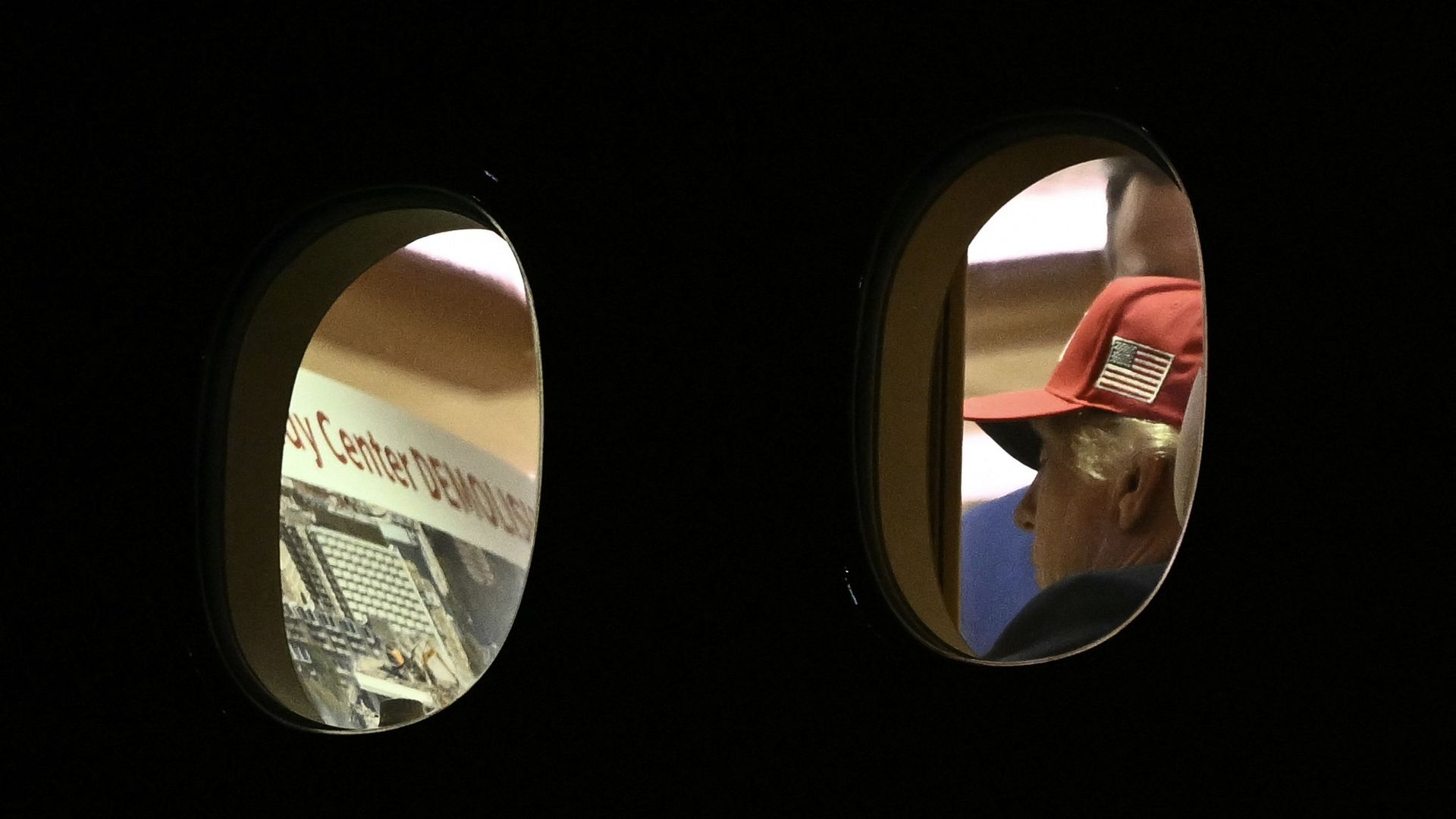 Two round mirrors mounted on a dark wall; the right mirror shows a person wearing a red baseball cap with an American flag patch, while the left mirror reflects part of a display or sign.