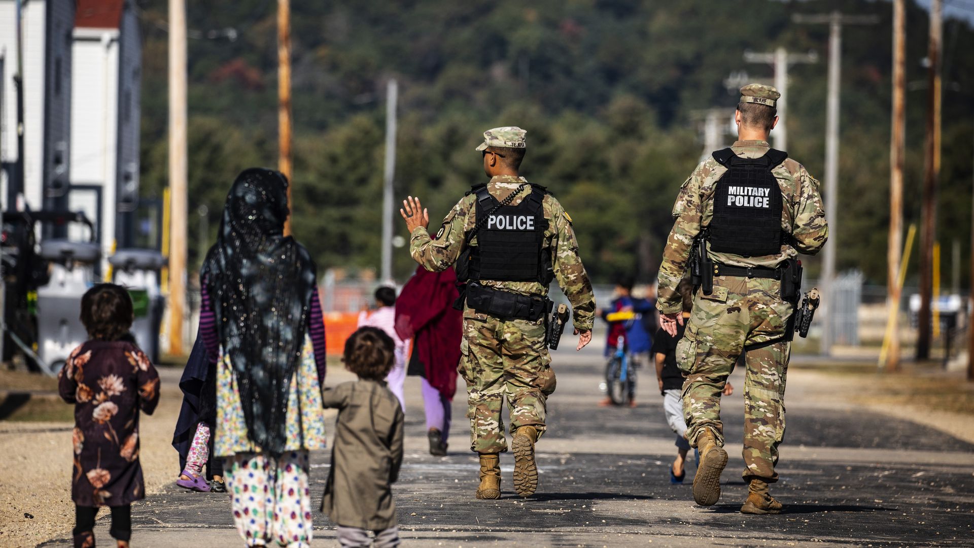 Military police wearing camouflage uniforms walk alongside a woman wearing a headscarf and two small children.
