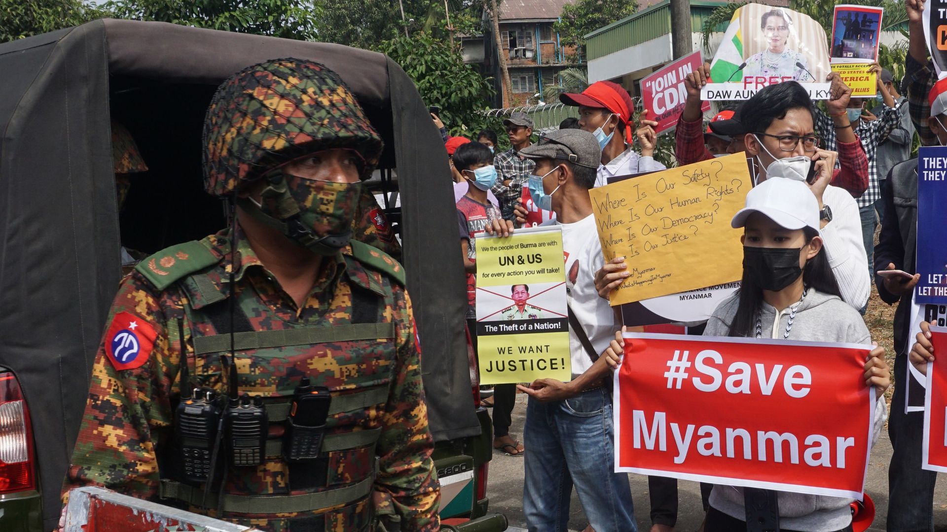 A soldier stands guard next to protesters holding signs during a demonstration against the military coup outside the Central Bank of Myanmar in Yangon on February 15
