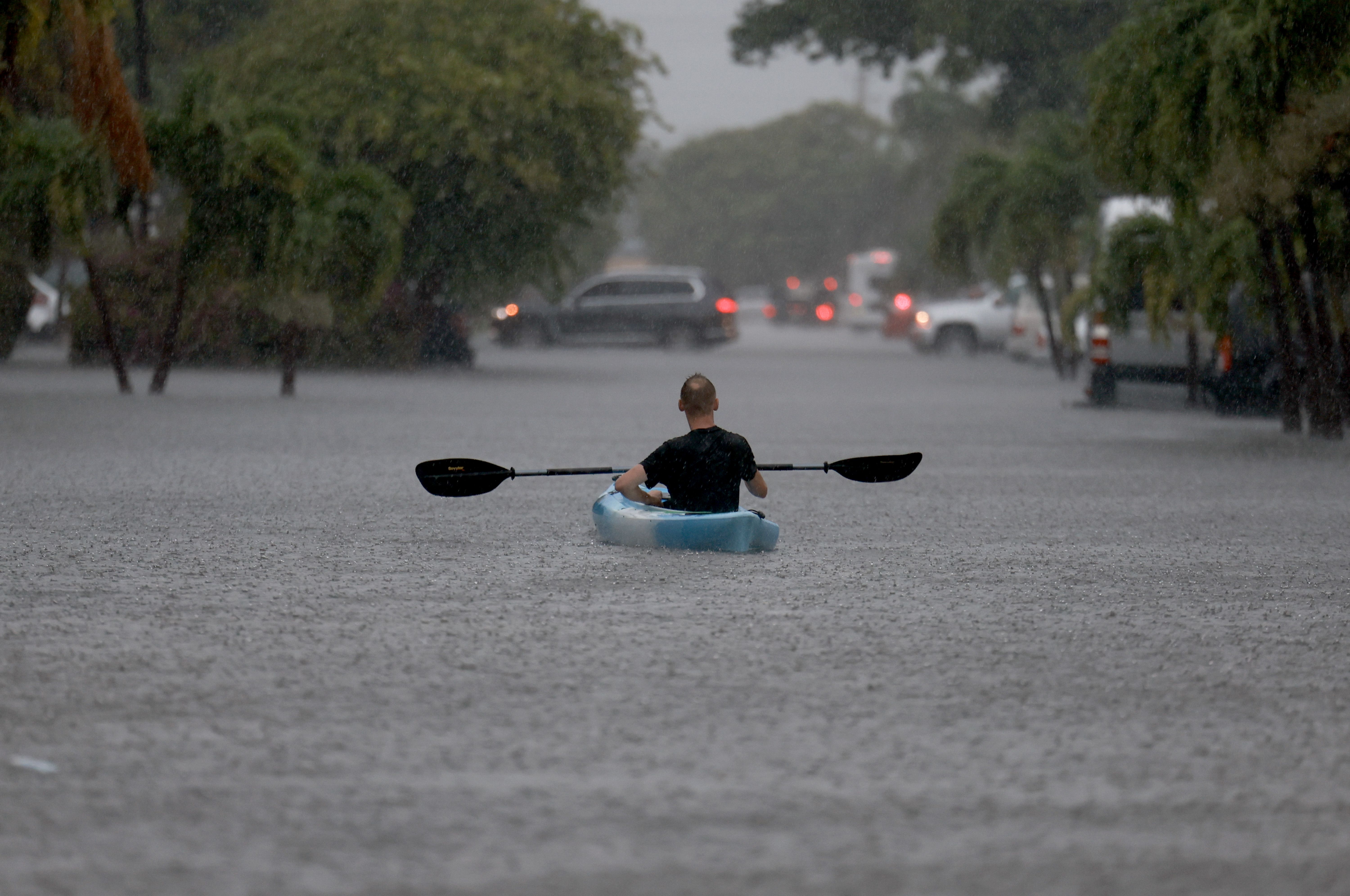 A person paddling a kayak down a road that's been flooded. 