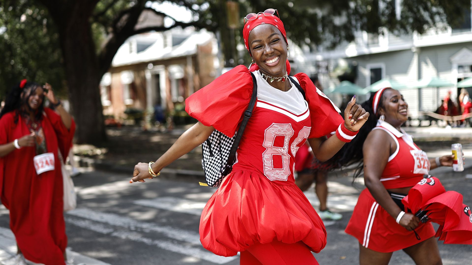 A woman smiles and poses midstride for the camera. She and the other runners around her wear bright ensembles.