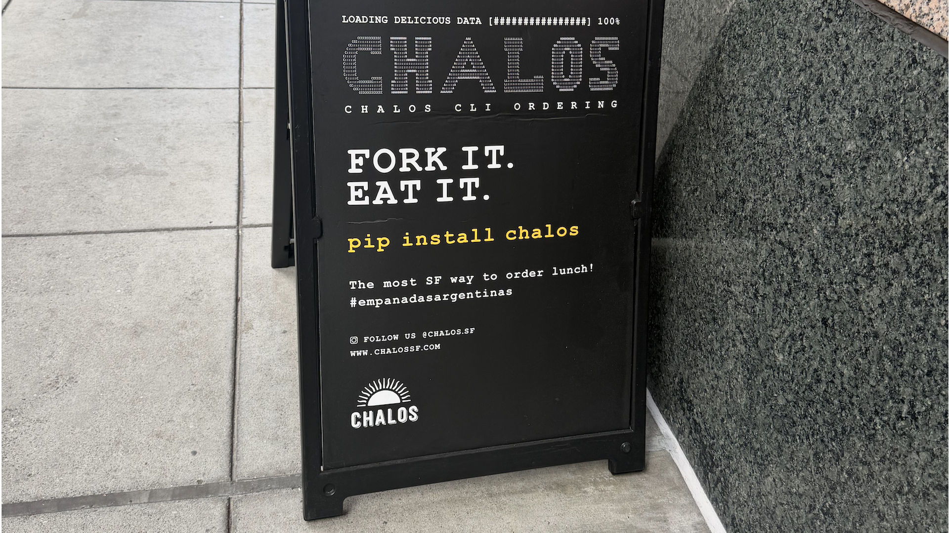 A black sidewalk sign outside a granite wall shows "LOADING DELICIOUS DATA [################] 100%", a large CHALOS graphic, and the white slogan "FORK IT. EAT IT." with yellow "pip install chalos" text.