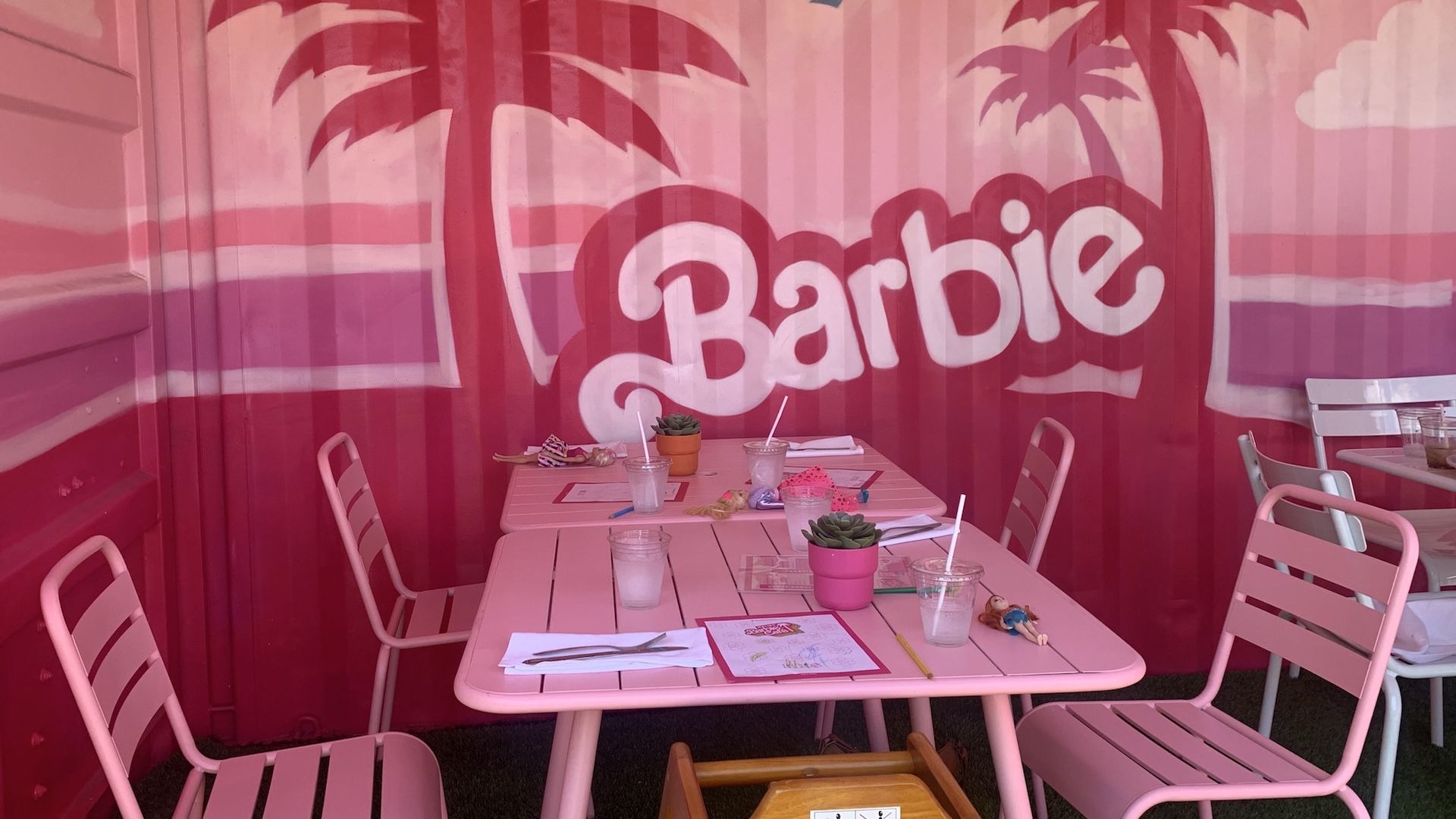 Pink table and chairs in front of pink and purple backdrop with two palm trees and the word Barbie.