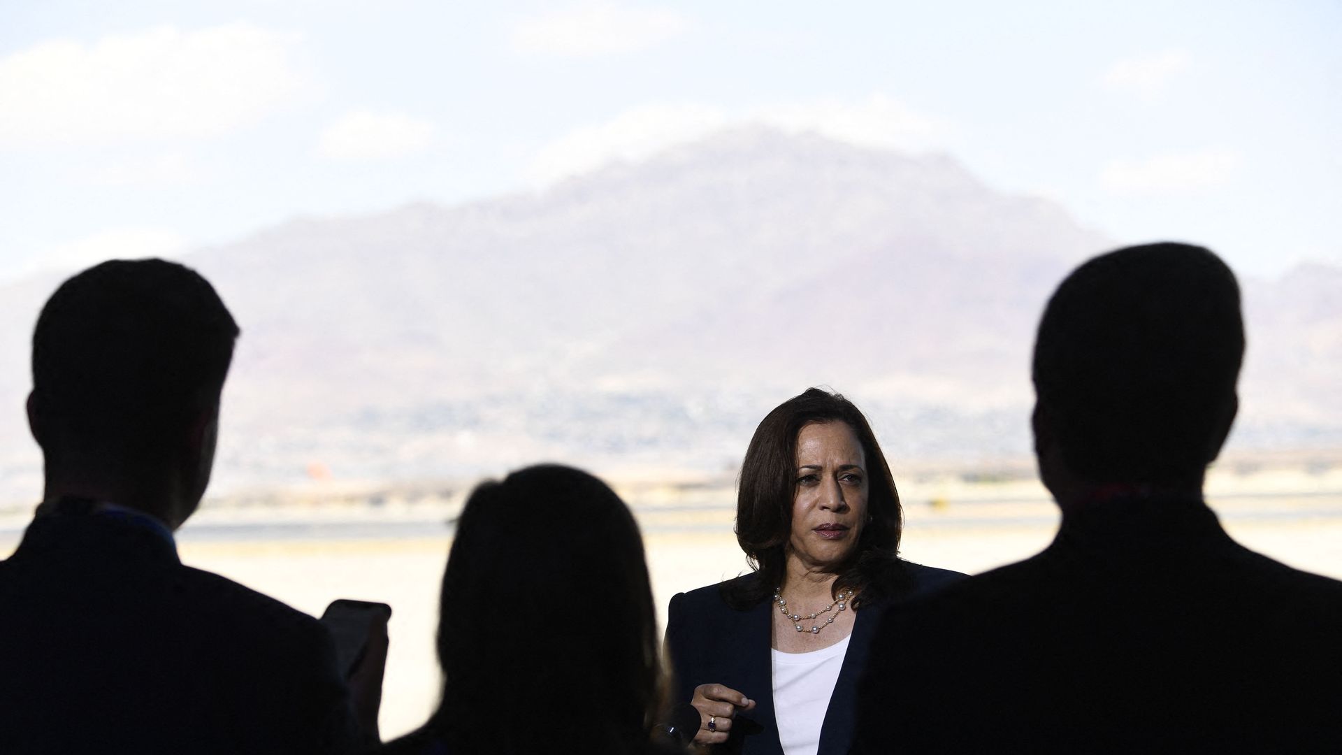 Kamala Harris talks with several people shadowed in the foreground, with a mountain behind her.