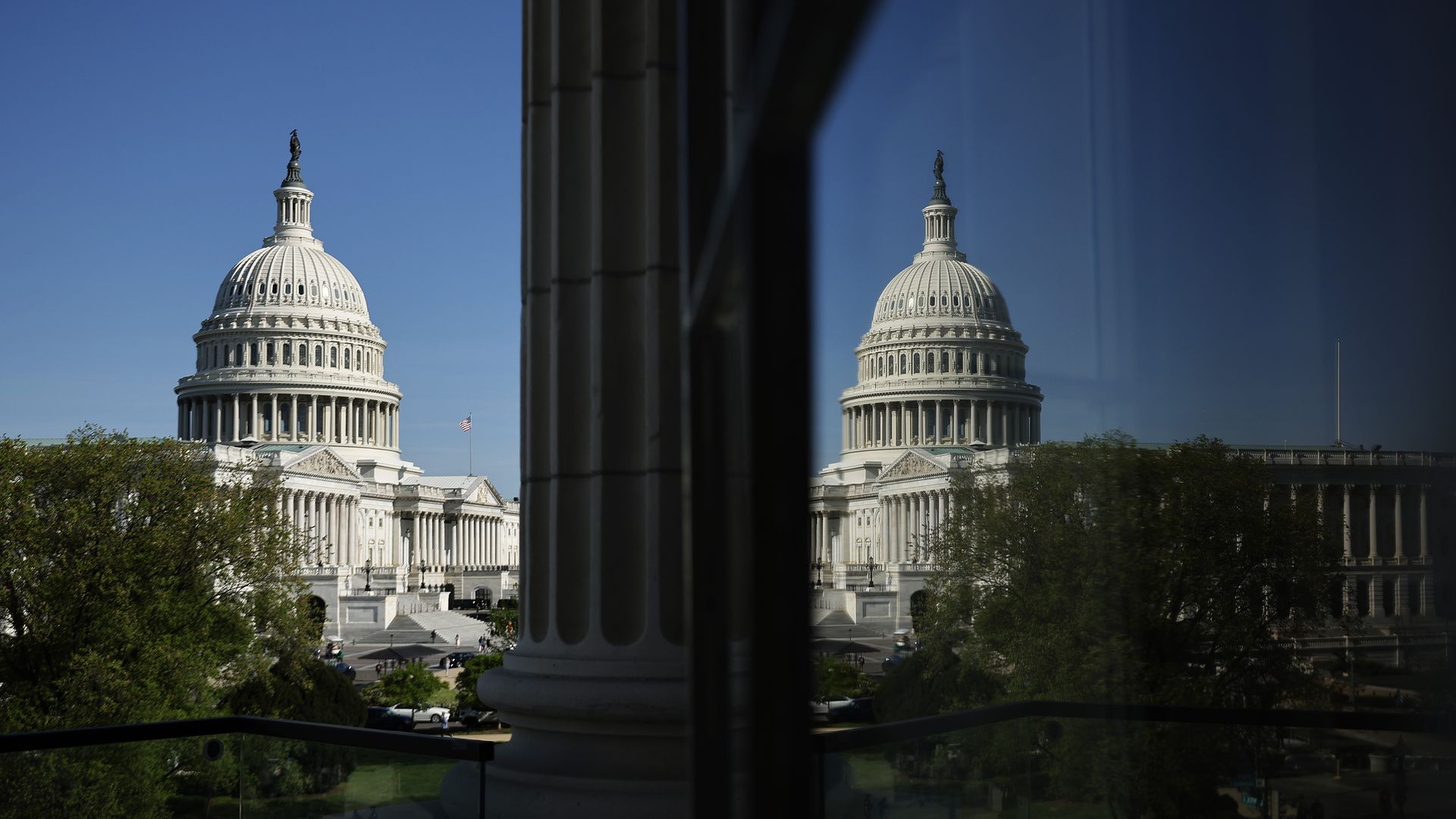 The U.S. Capitol and its reflection seen from a House office building on a sunny day.