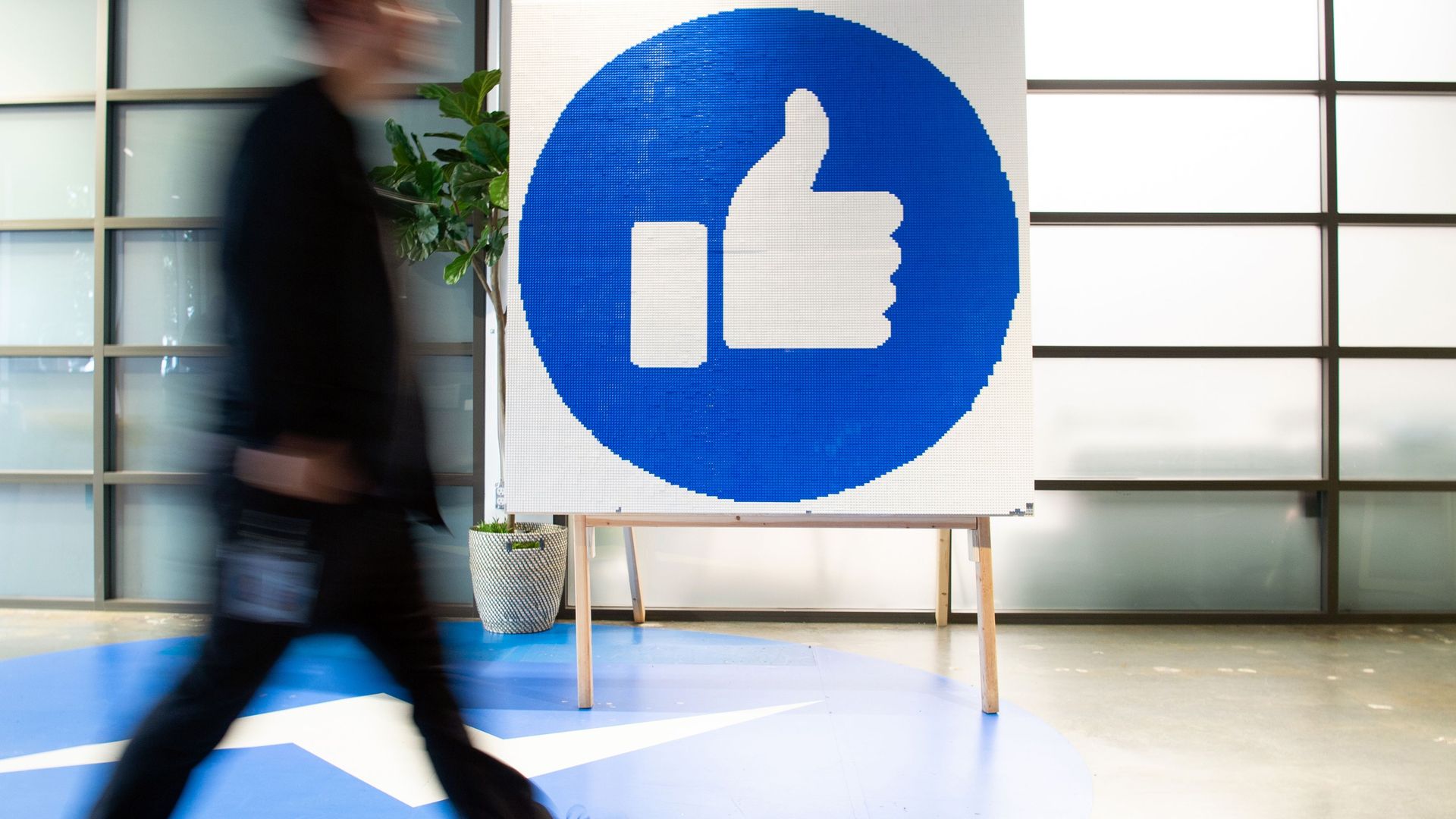 Photo of a sign showing the Facebook thumbs up emoji as a person walks by