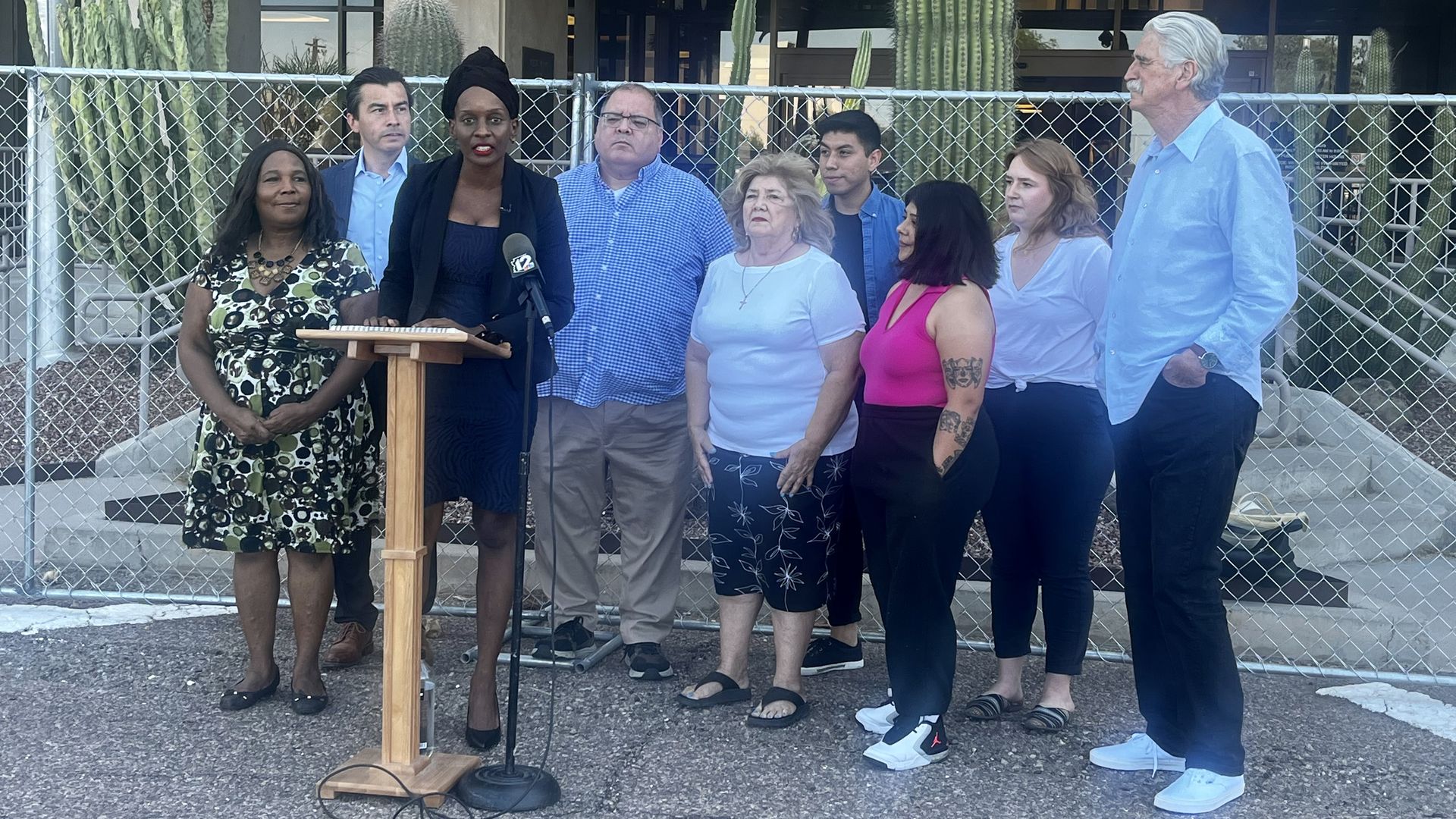 A group of people stand around a woman at a podium.