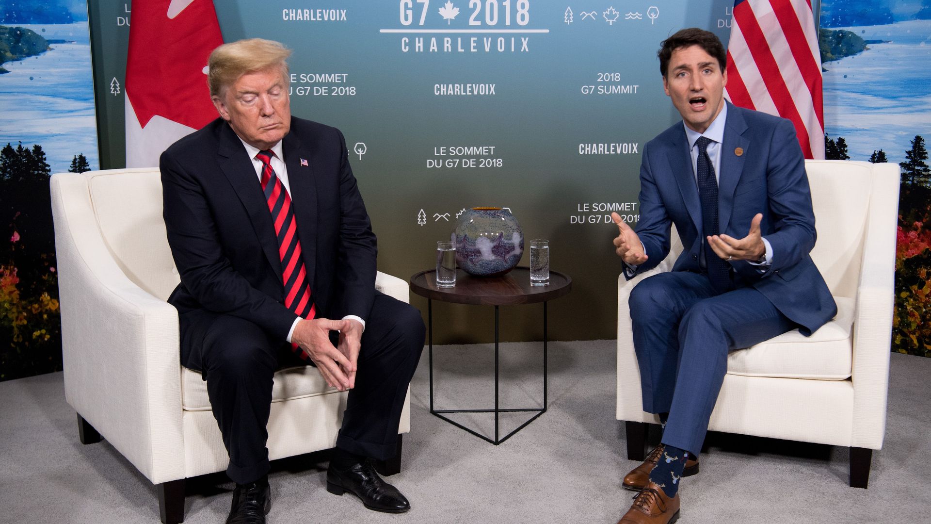 Canadian prime minister Justin Trudeau and Donald Trump sit on white chairs at the G-7 summit. Trump looks at the ground and appears unhappy, while Trudeau is talking with his mouth open and hands up
